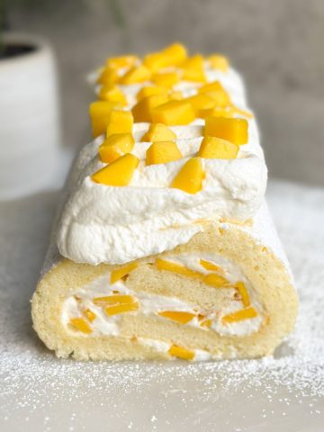 mango and cream swiss roll decorated with whipped cream and chopped mangoes. picture from the front SHOWING THE CROSS SECTION WITH A SWIRL OF CAKE AND CREAM