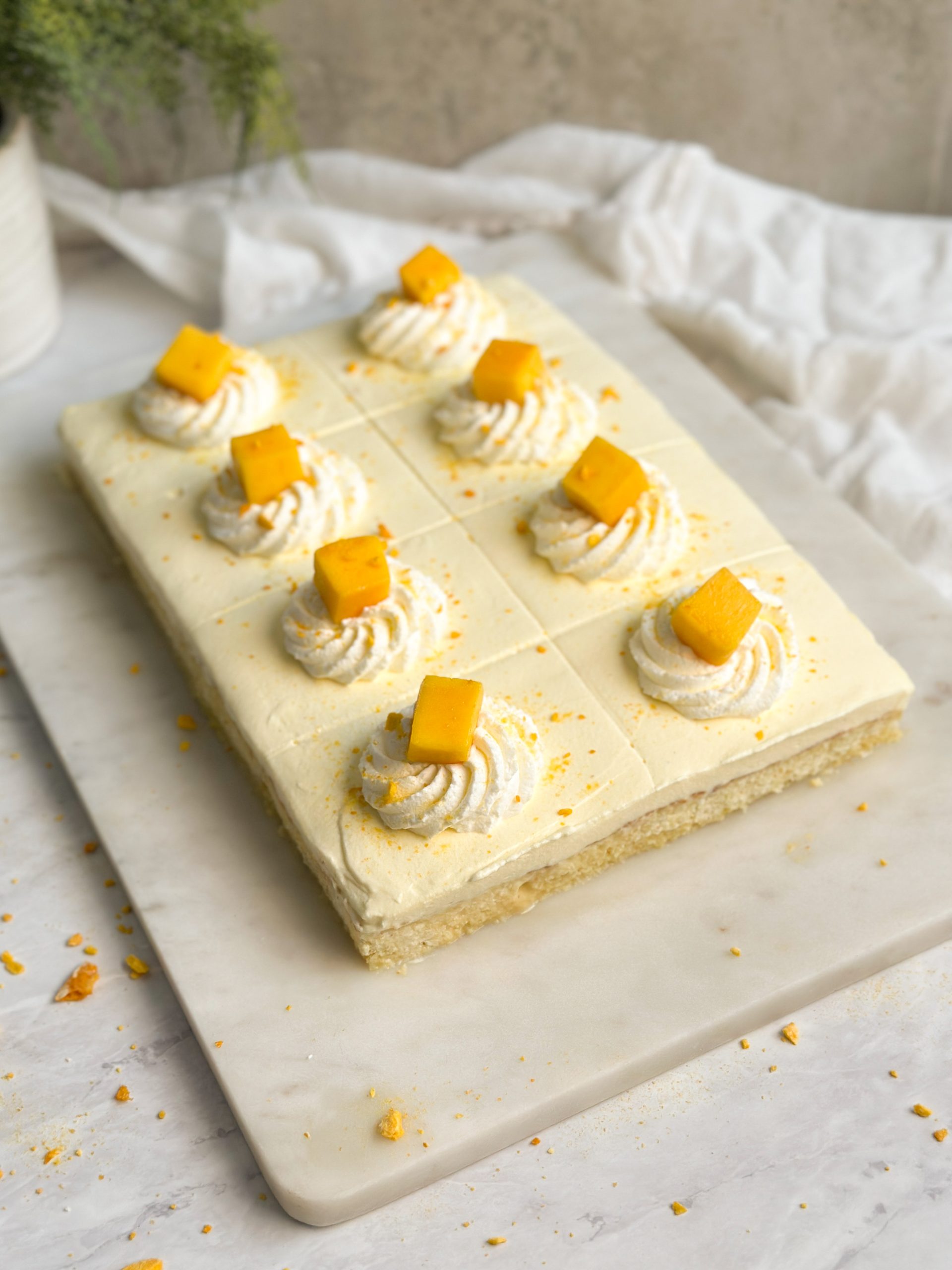 A sheet of mango lassi tres leches cake decorated with mango whipped cream, whipped cream rosettes and mango cubes