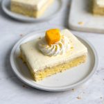 a slice of mango lassi tres leches cake on a plate with a moist interior, thick layer of mango lassi whipped cream, and whipped cream and mango decoration