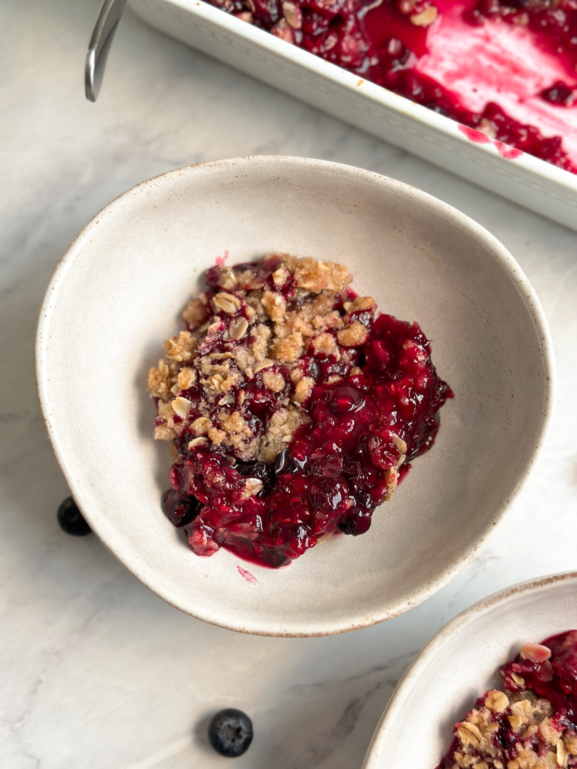 berry crumble in a bowl with a crispy oat crumble and bubbling berries underneath