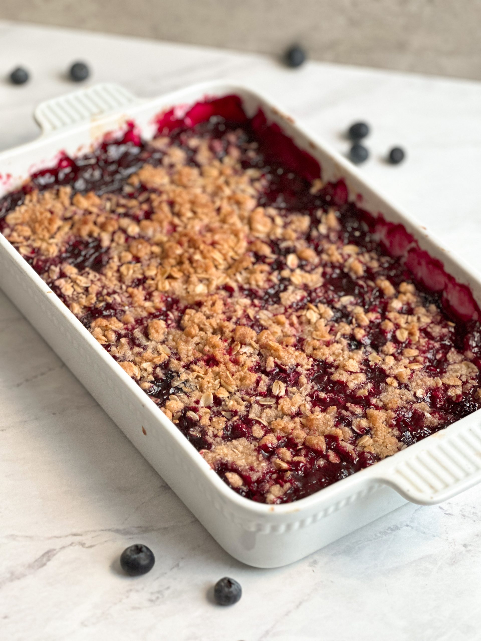 triple berry crumble in a white casserole dish with golden crispy oat crumble topping and berries bubbling through it