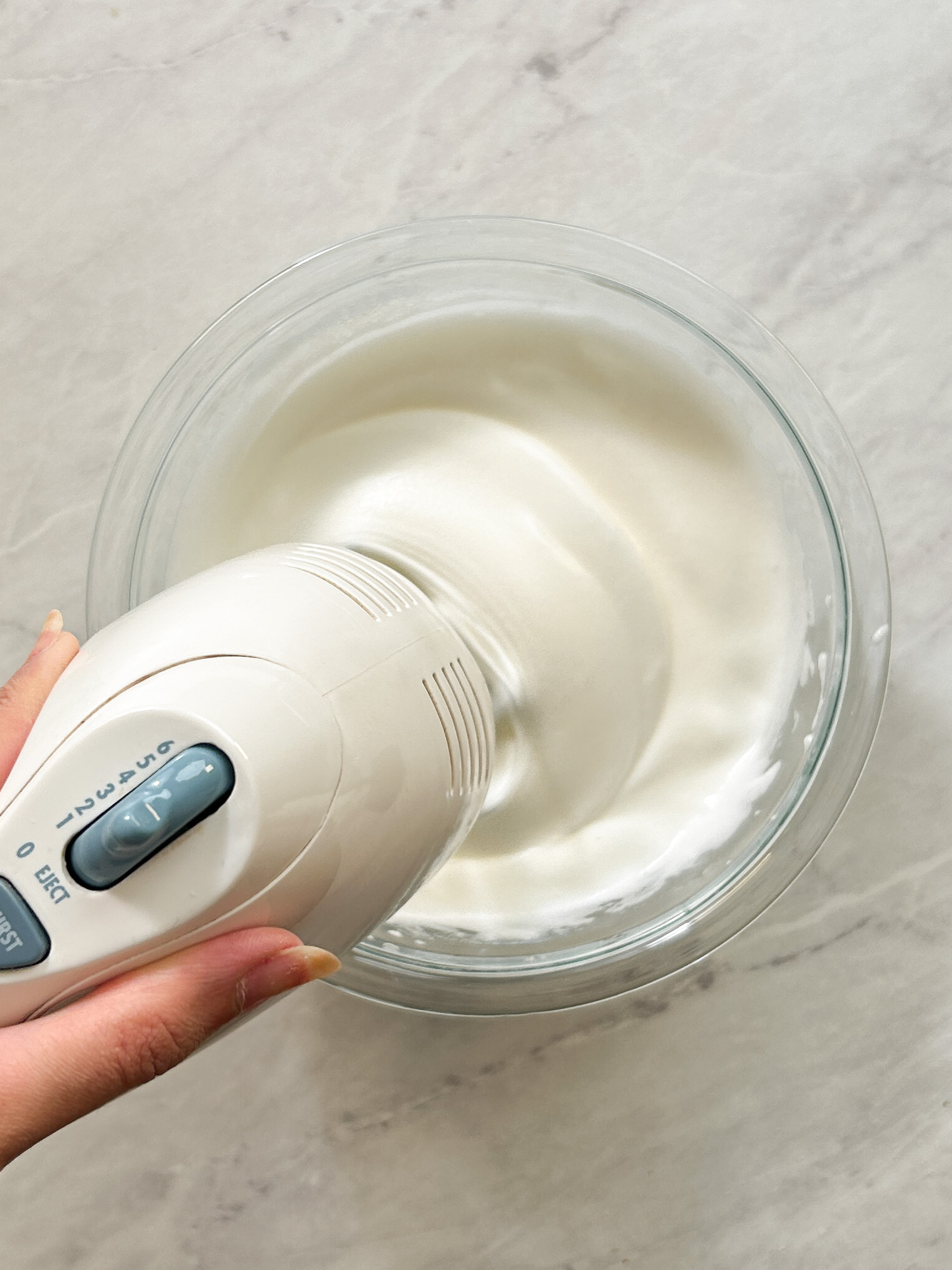 hand mixer whisking egg whites with sugar in a glass bowl
