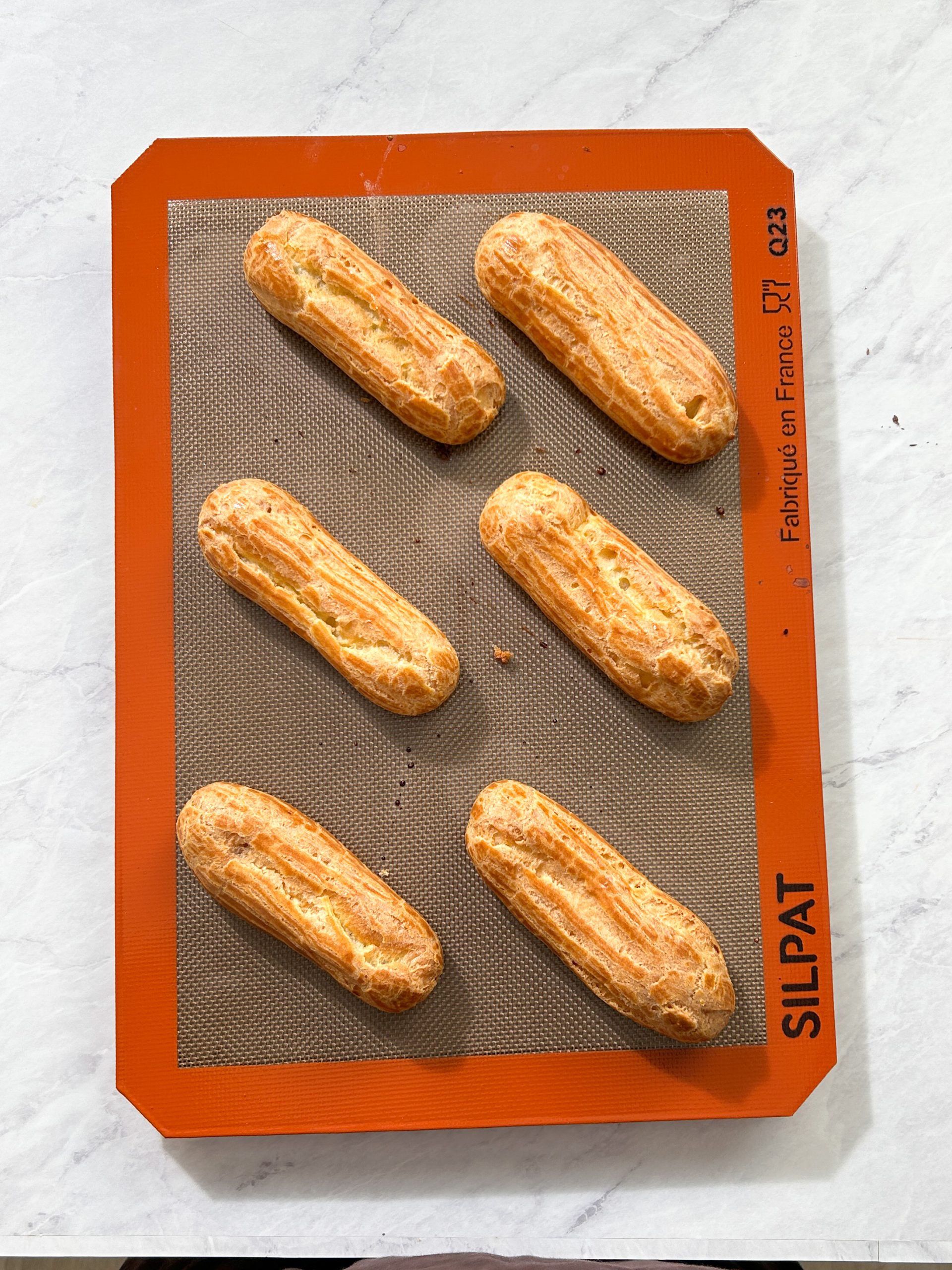 6 baked eclairs with golden brown color on baking sheet