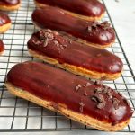 5 eclairs placed sideways on a wire rack; golden color and shiny chocolate glaze on top