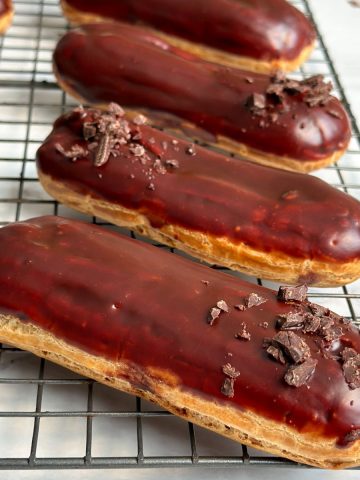 5 eclairs placed sideways on a wire rack; golden color and shiny chocolate glaze on top
