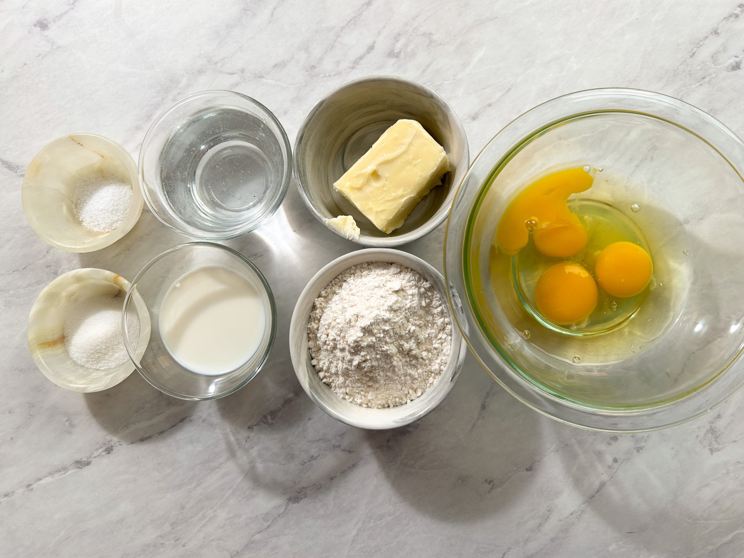 overhead image of ingredients needed to make eclairs: butter, eggs, water, milk, flour, sugar and salt