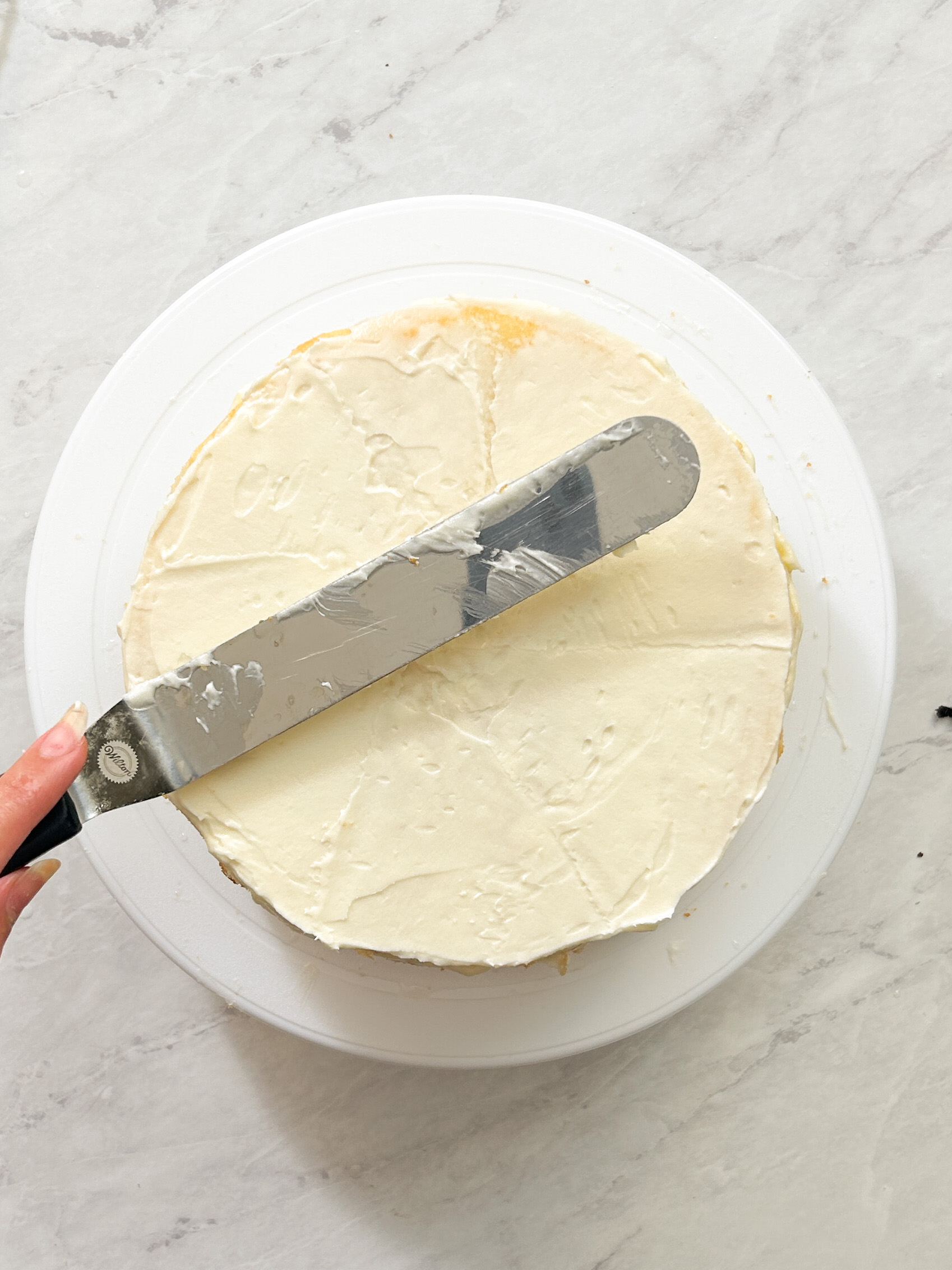 cream cheese frosting being spread on a layer of cake during assembly