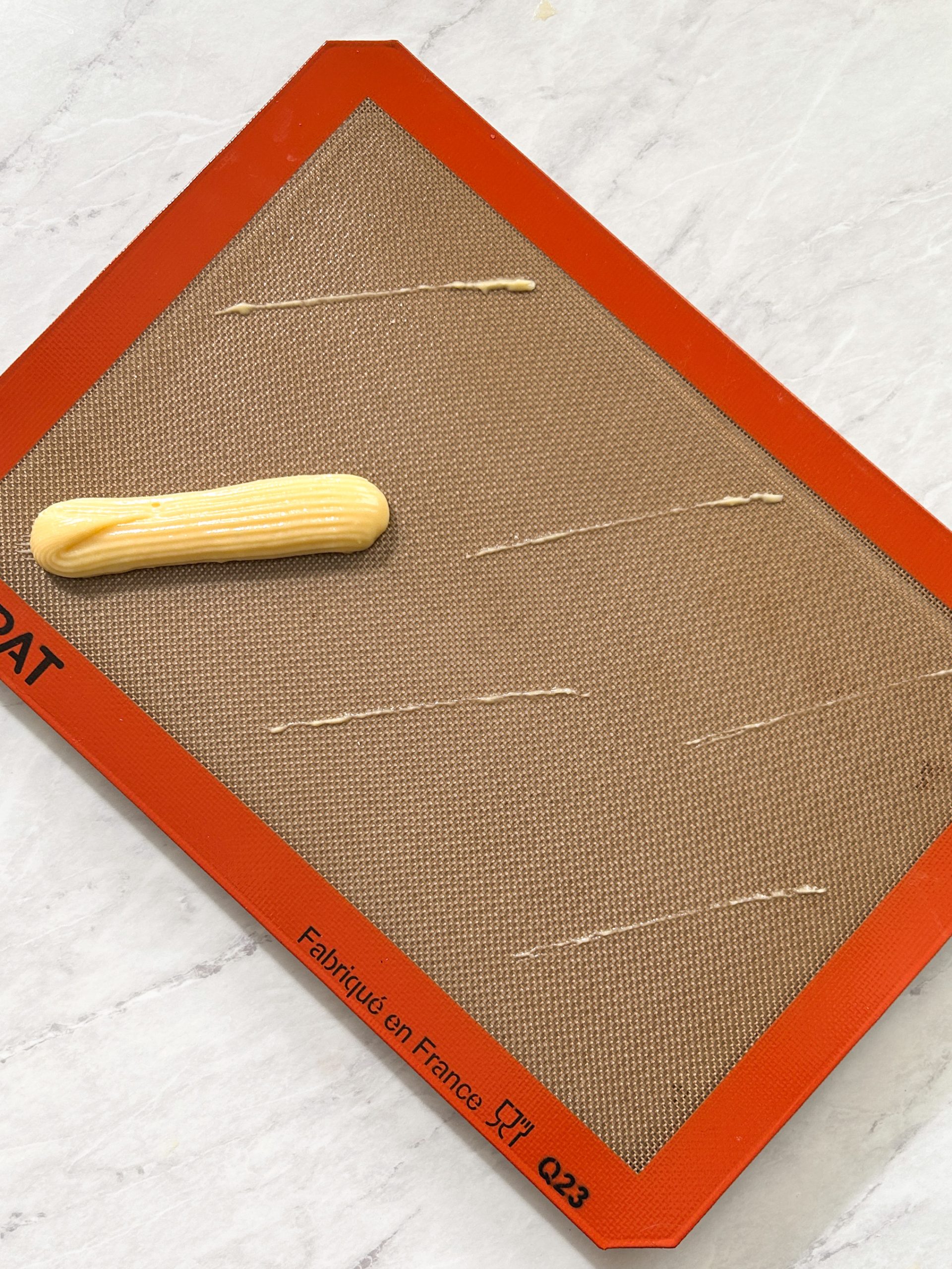 one eclair pipped onto a silicon baking mat