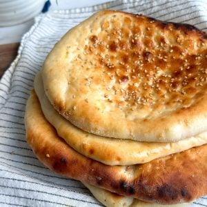 pile of 4 roghni naans on a tea towel. Naans have a beautiful golden color and sesame seeds on them