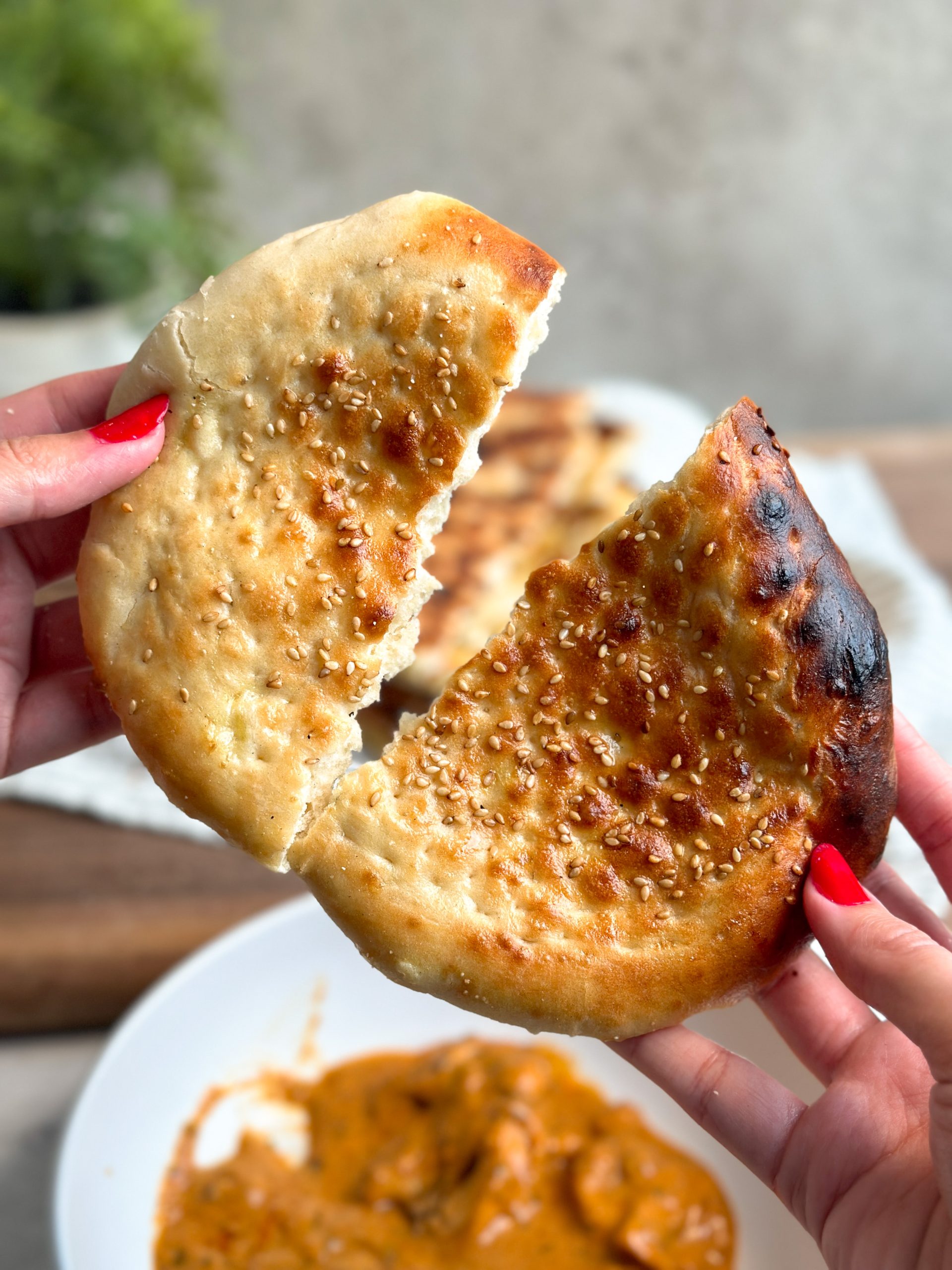 one soft and golden roghni naan being torn into half by 2 hands revealing their soft texture 