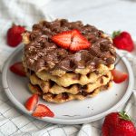 4 Belgian liege waffles stacked on a plate, drizzled with Nutella and covered with chopped strawberries