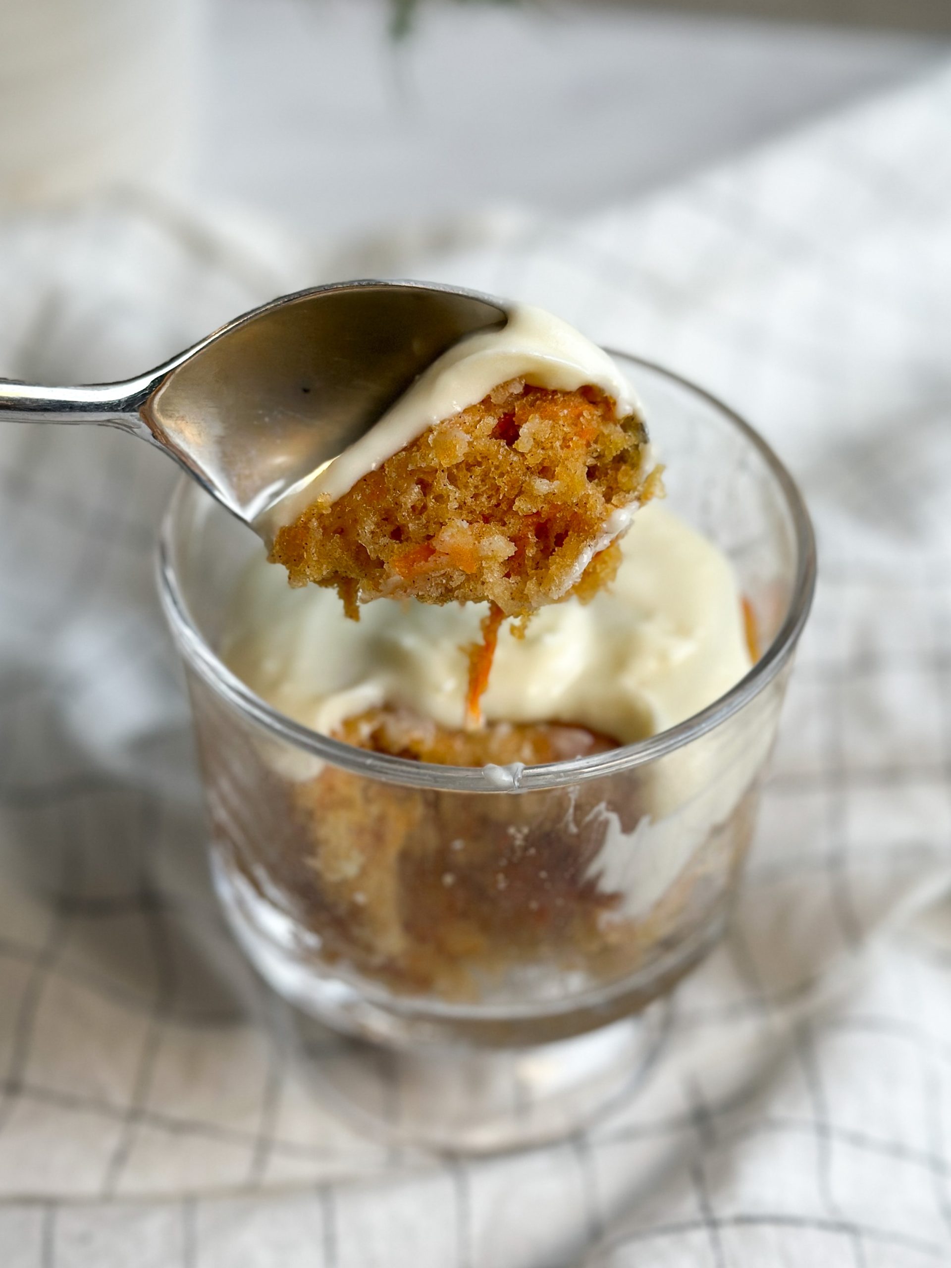 carrot mug cake in a glass mug with a spoon taking out a bite revealing soft moist interior