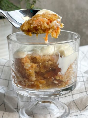 carrot mug cake in a glass mug with a spoon taking out a bite revealing soft moist interior
