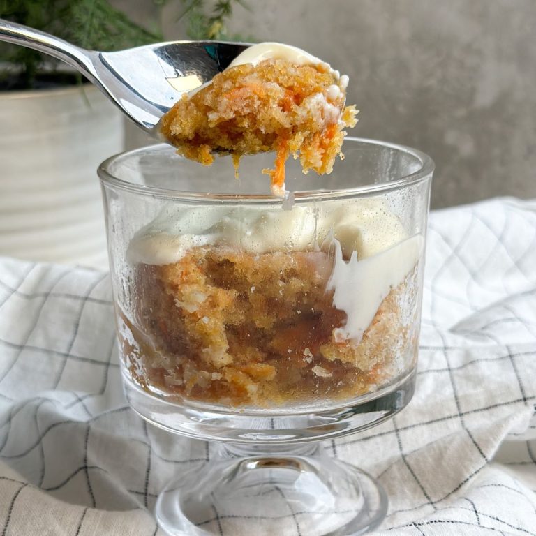 carrot mug cake in a glass mug with a spoon taking out a bite revealing soft moist interior