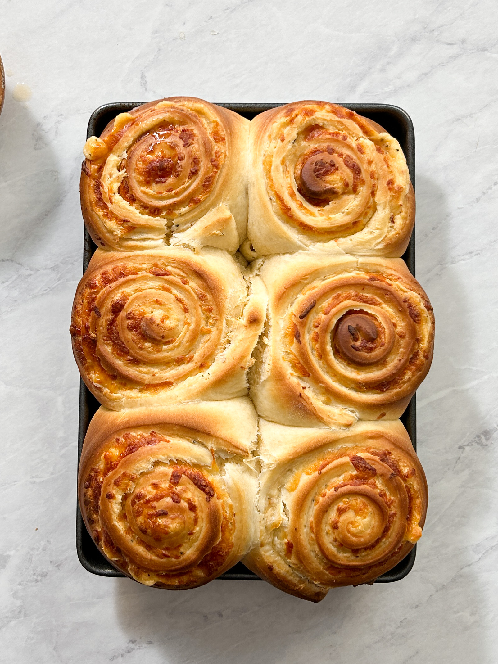 6 baked cheesy bread rolls in a small sheet pan. rolls are soft, filled with cheese, and golden