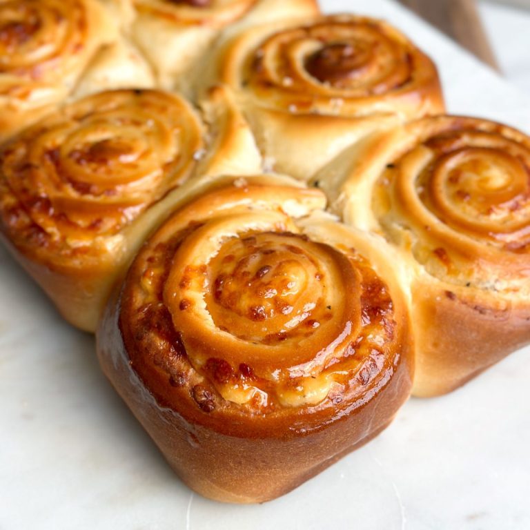 side angle of 6 cheesy bread rolls side by side on a serving board with a beautiful golden color and honey butter spread on top