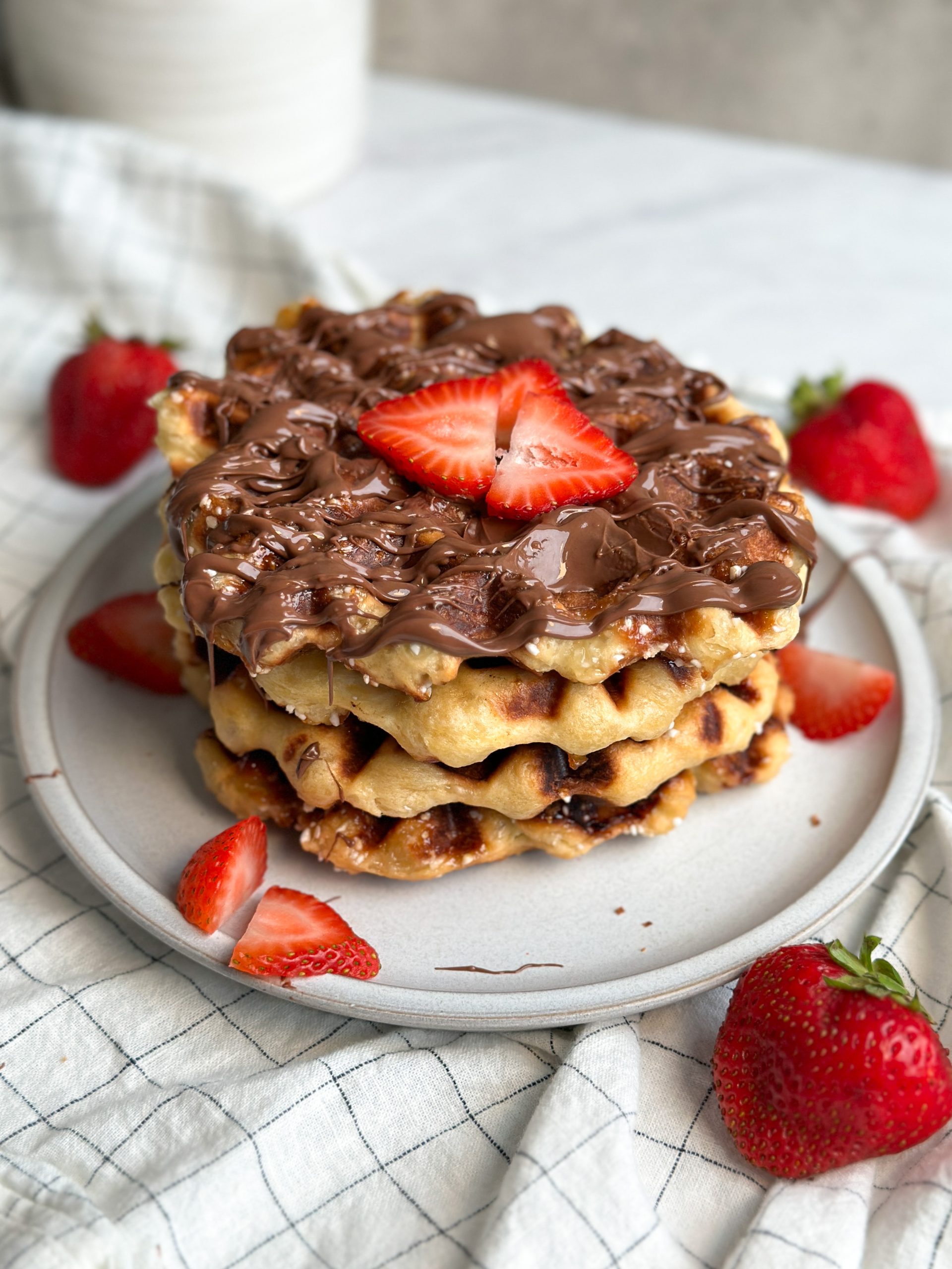 4 Belgian liege waffles stacked on a plate, drizzled with Nutella and covered with chopped strawberries
