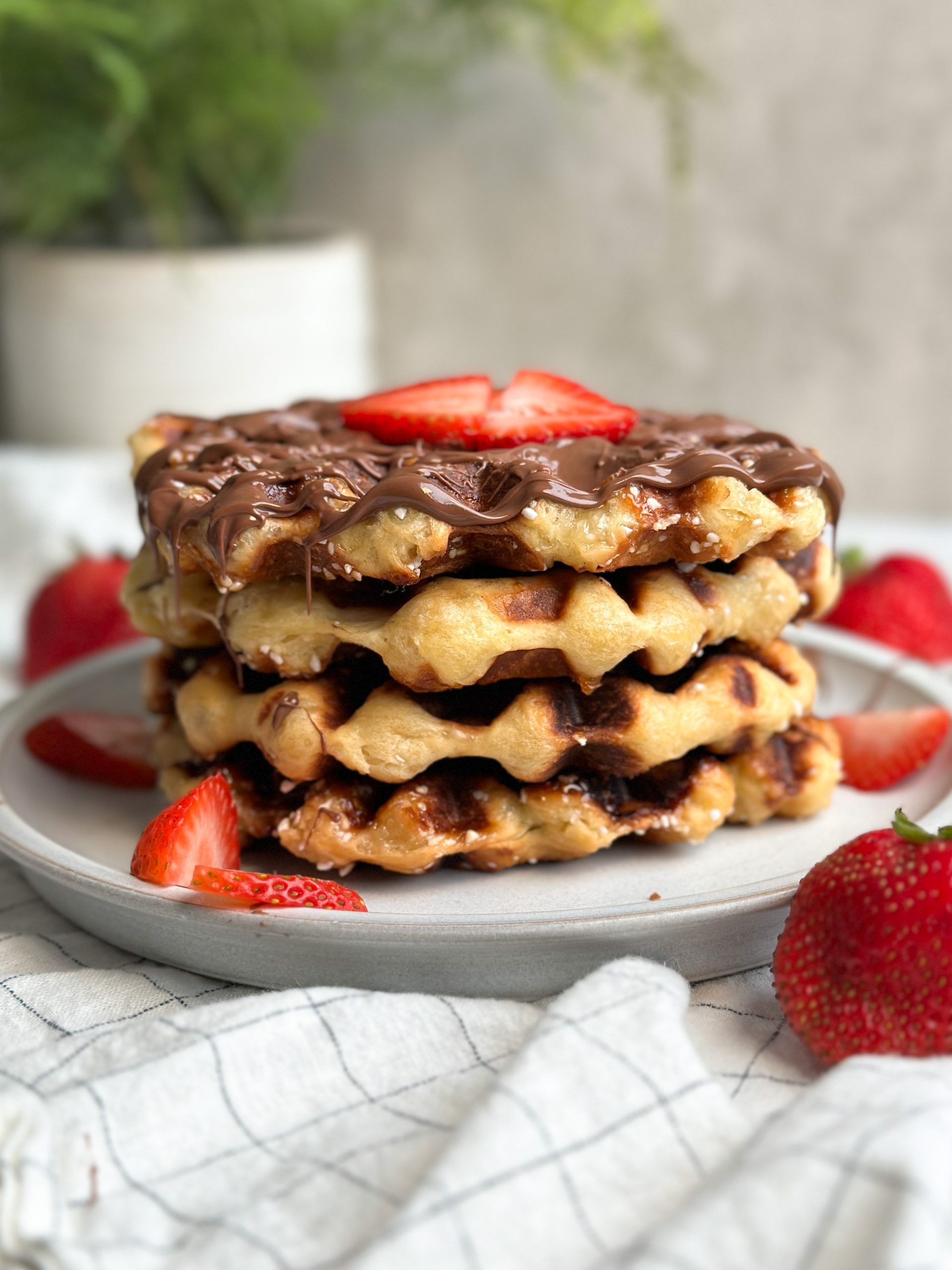 Side image of 4 Belgian liege waffles stacked on a plate, drizzled with Nutella and covered with chopped strawberries