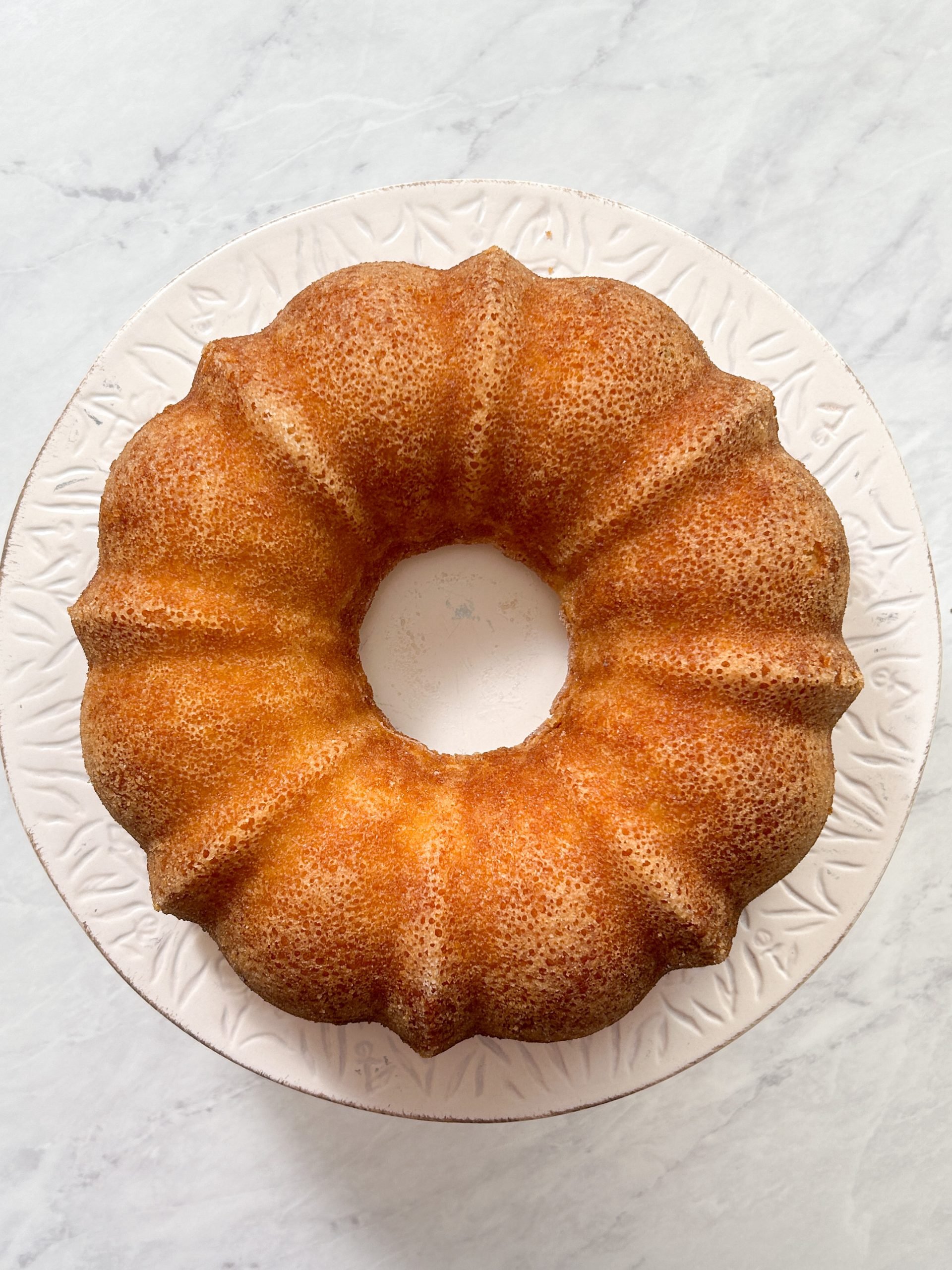 bundt cake on a serving stand. cake has a beautiful golden crust on the outside