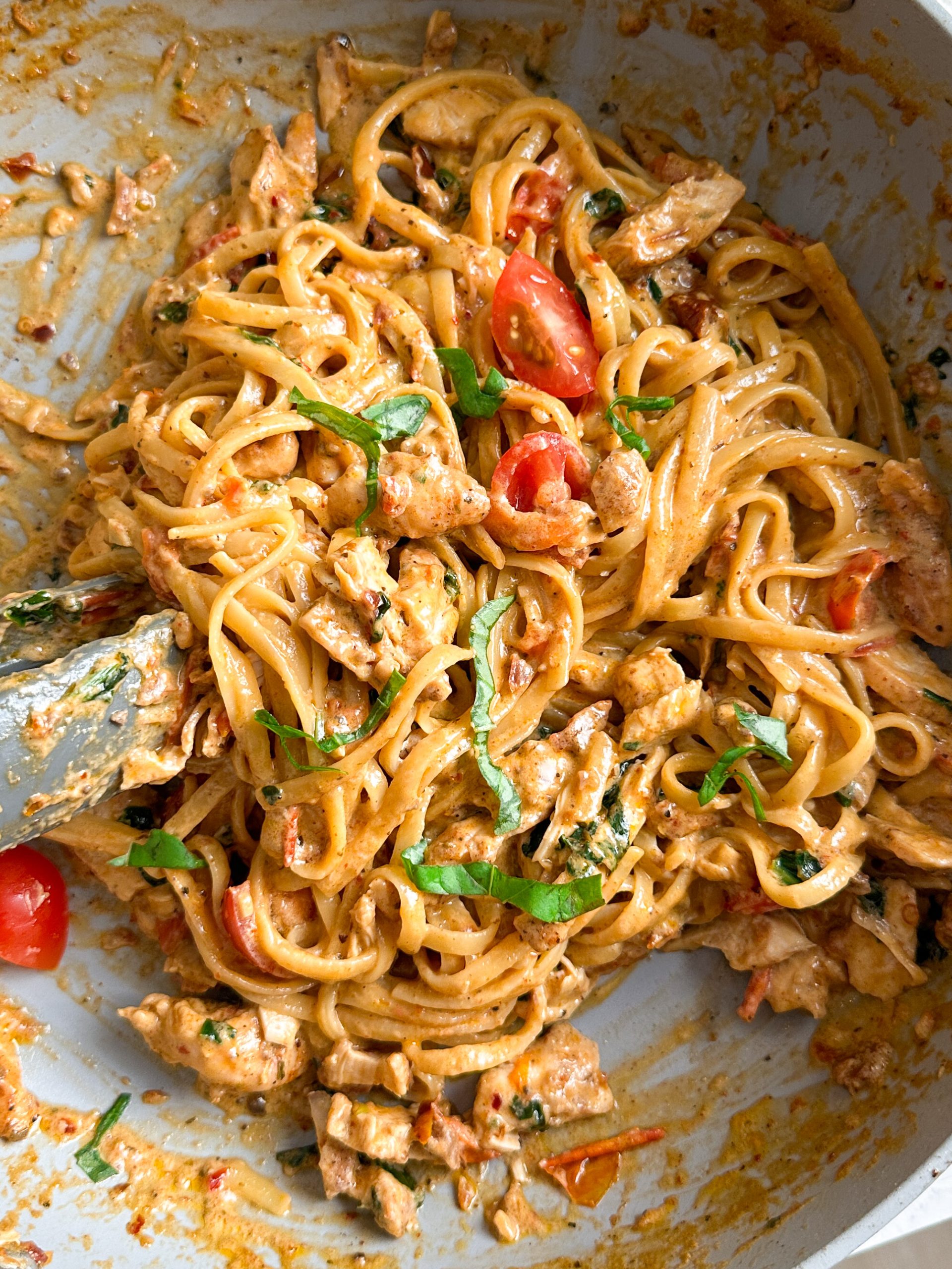 close up of creamy tuscan chicken pasta with chopped basil and cherry tomatoes on top