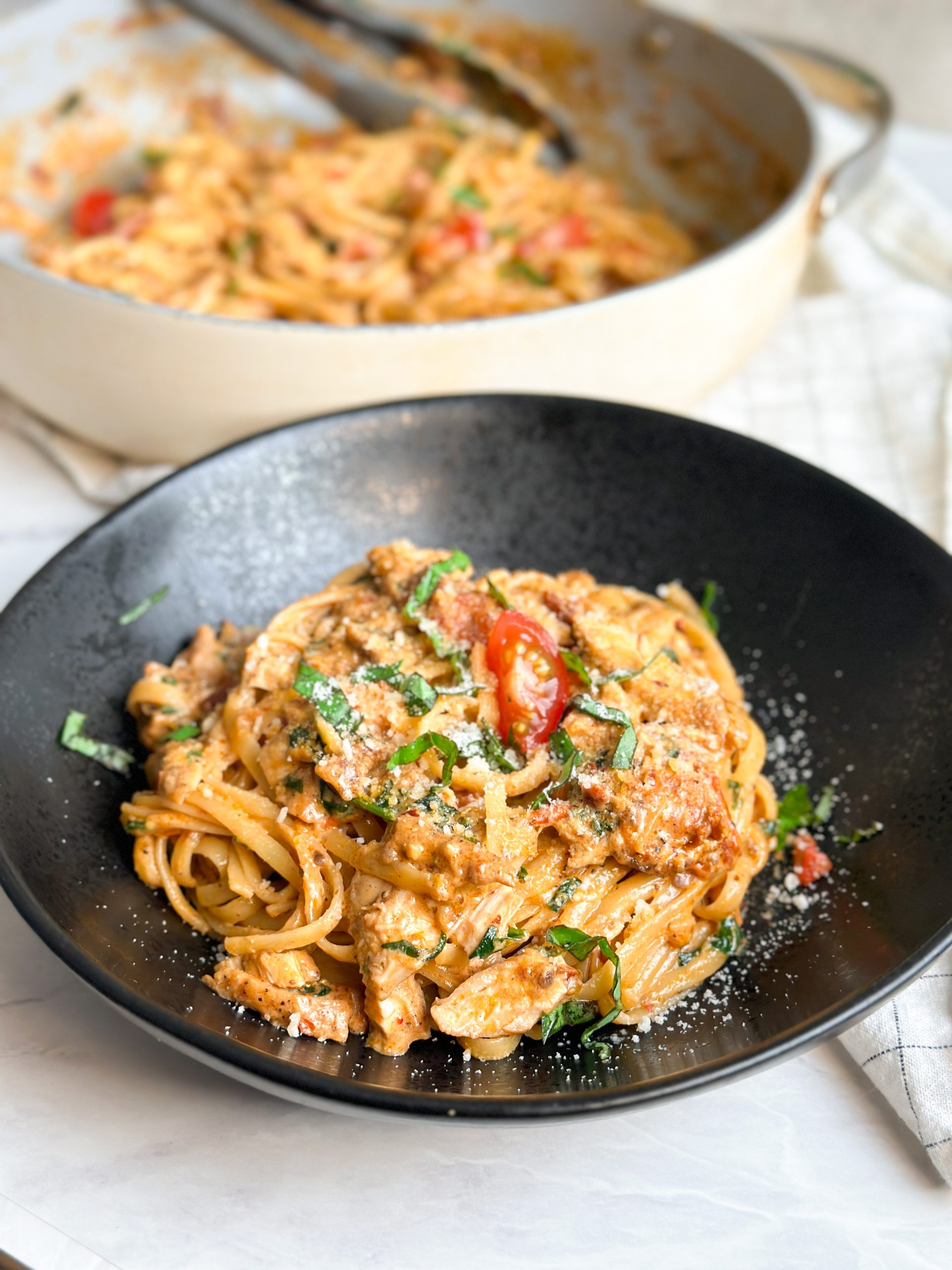 creamy tuscan chicken pasta in a black plate garnished with basil leaves