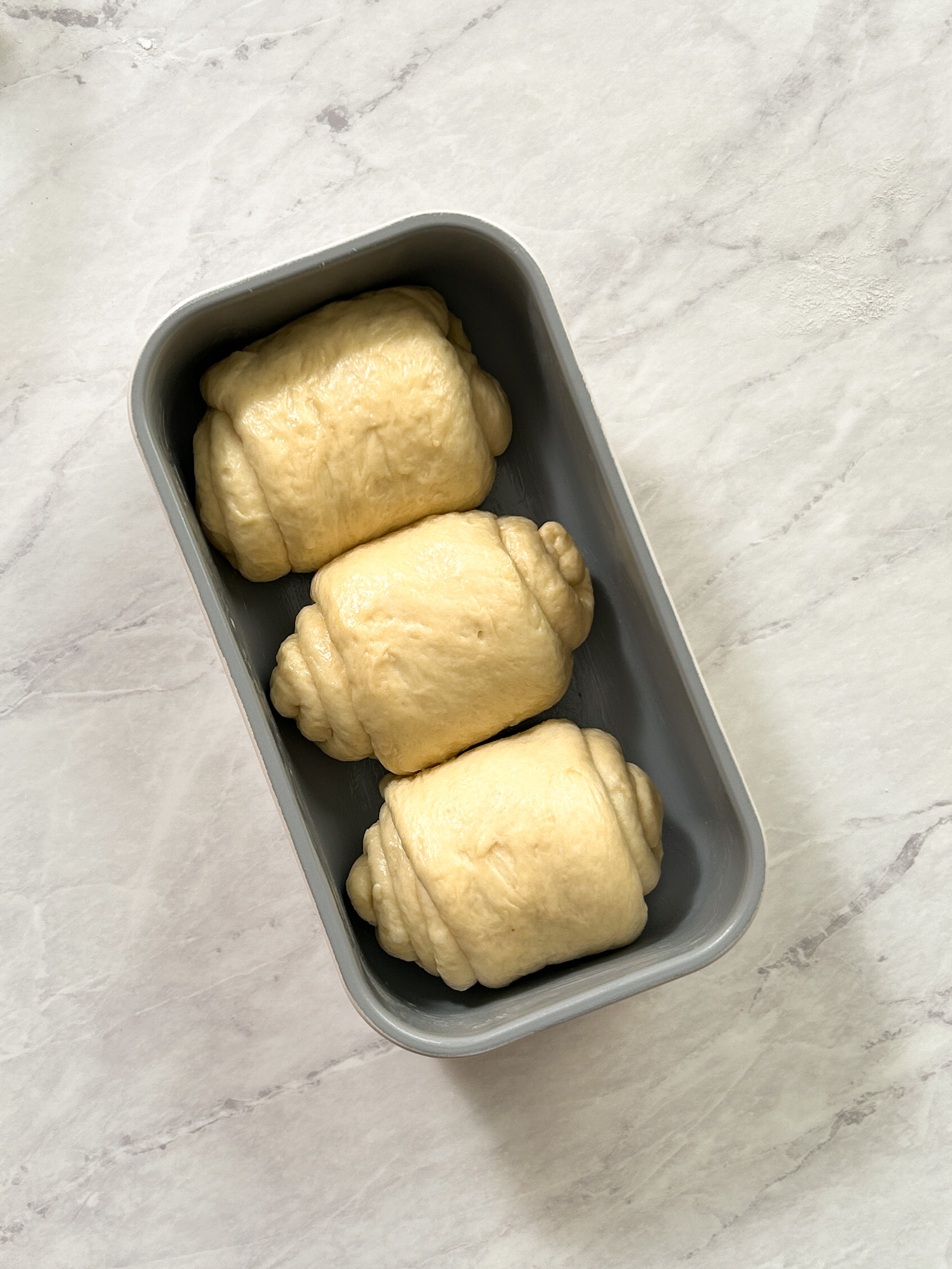 3 rolls of dough in a bread loaf pan before proofing