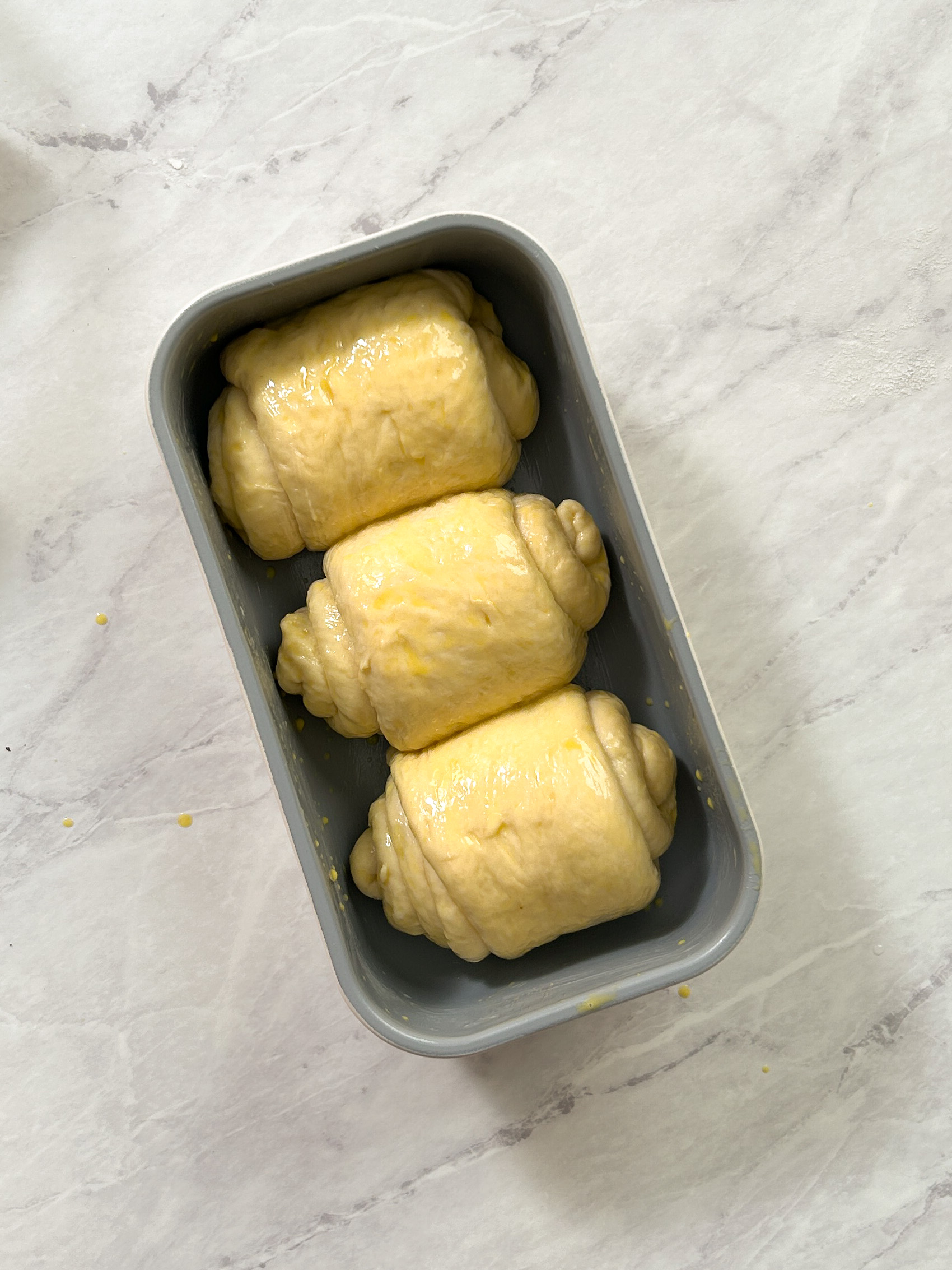 three rolls of dough in a loaf pan with a layer of egg wash on them