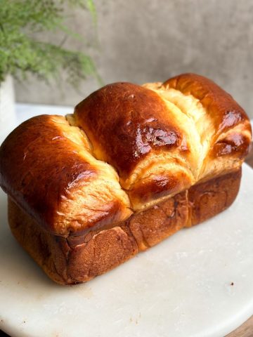 a loaf of japanese milk bread on a marble serving board. loaf has a beautiful golden shine all over and three pieces coming together