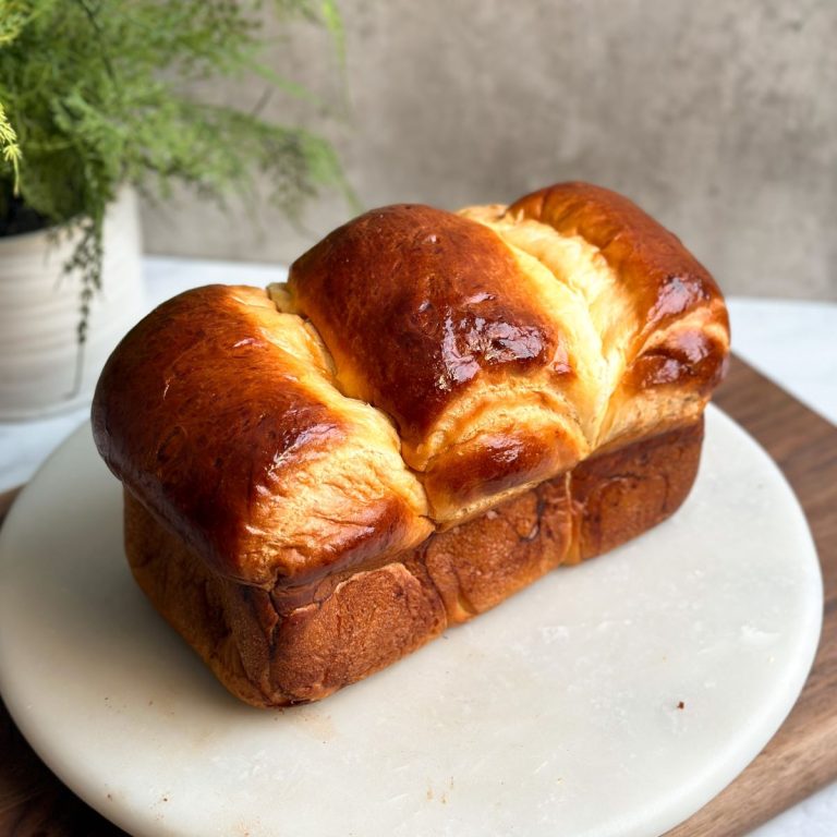 a loaf of japanese milk bread on a marble serving board. loaf has a beautiful golden shine all over and three pieces coming together