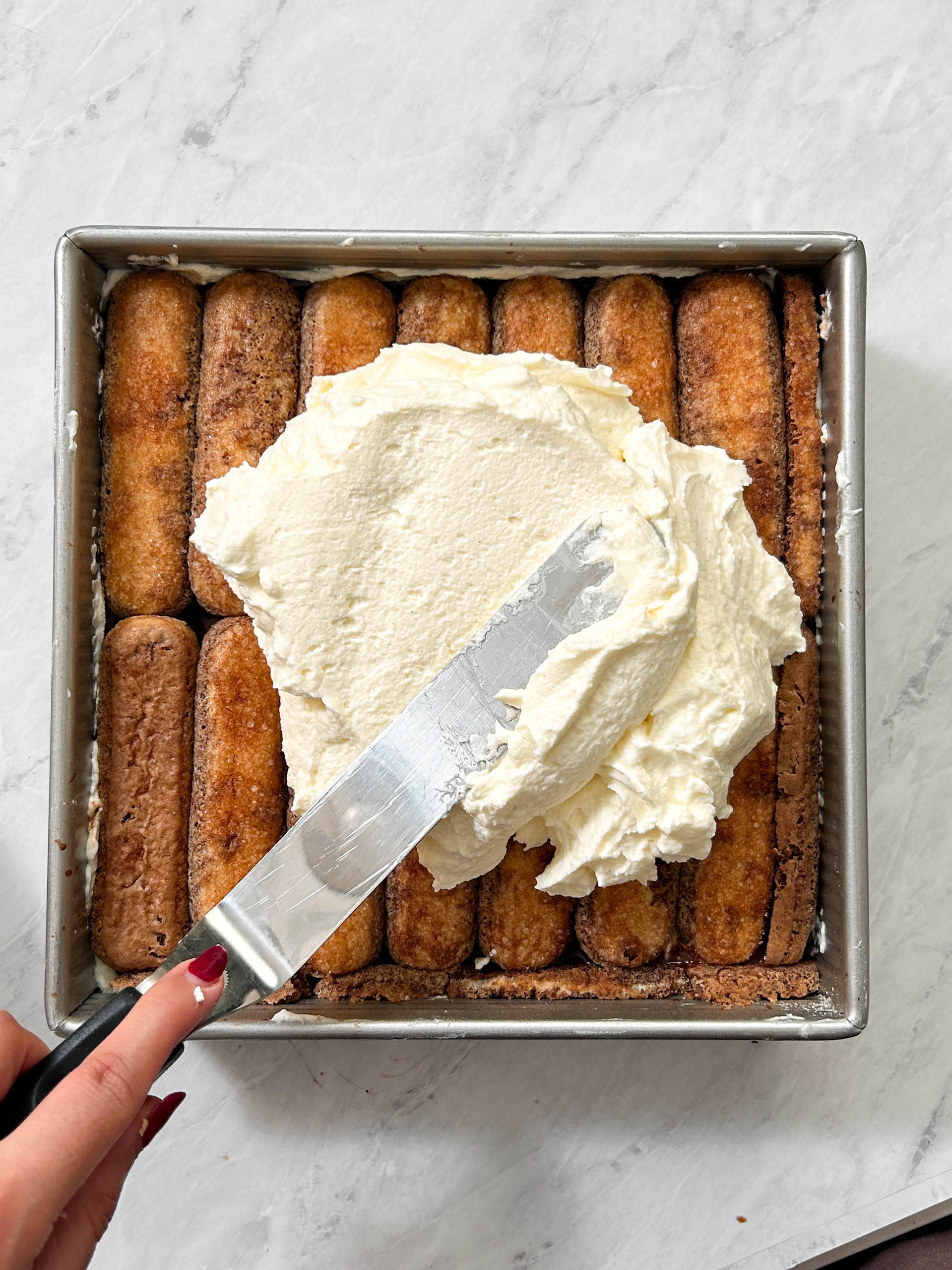 offset spatula spreading a layer of mascarpone cream on top of a layer of ladyfingers