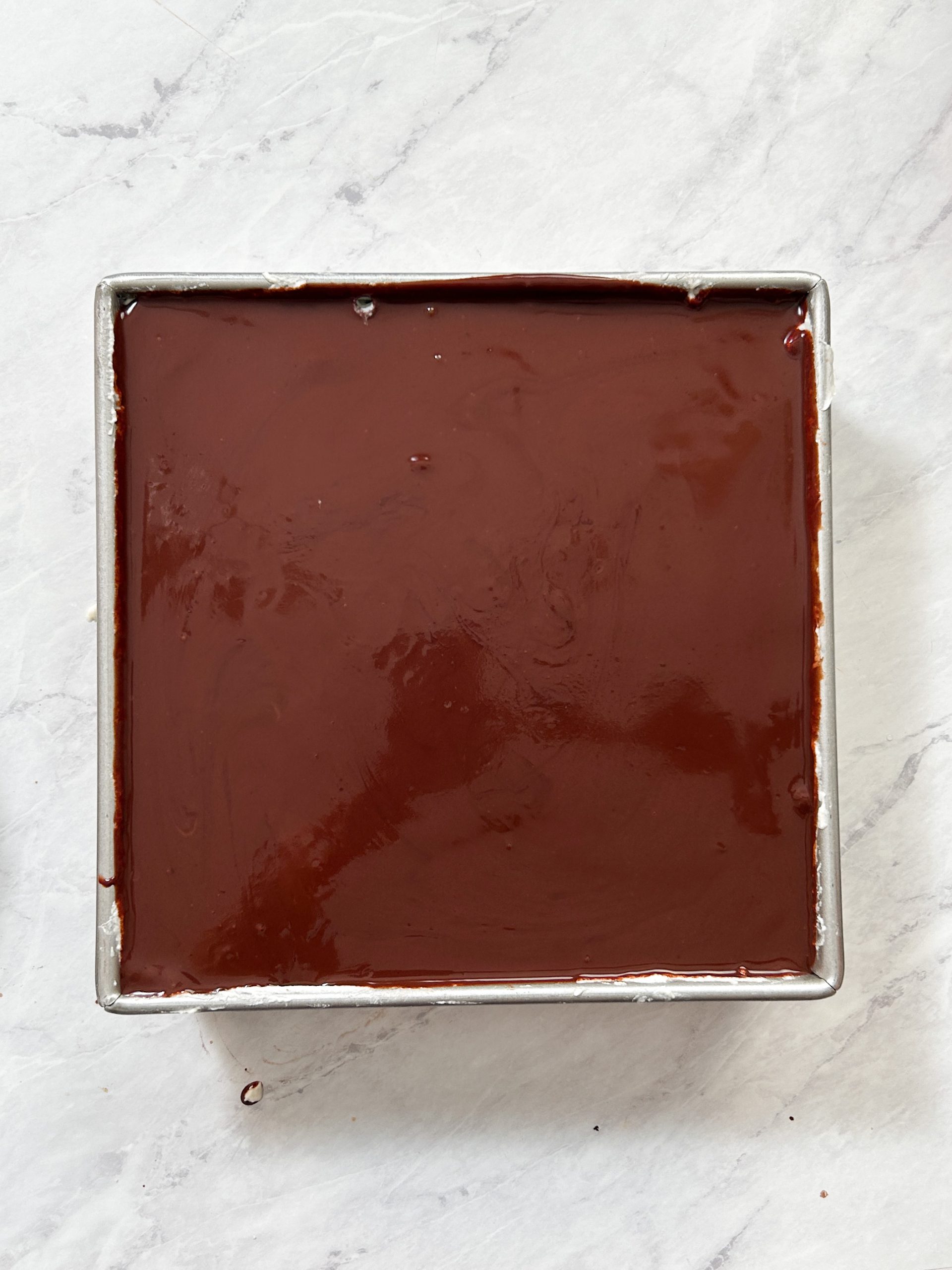 chocolate tiramisu in a pan topped with shiny chocolate ganache