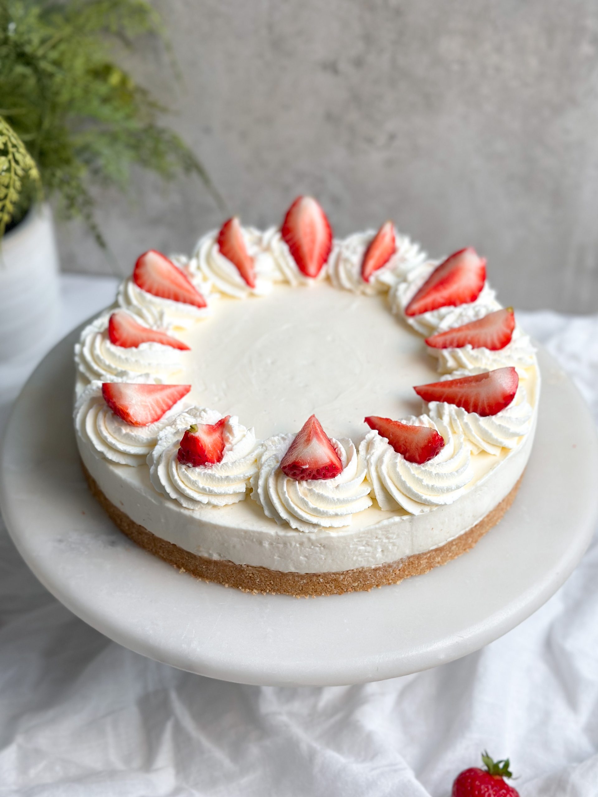 a no bake cheesecake on a marble serving board decorated with whipped cream and fresh strawberries