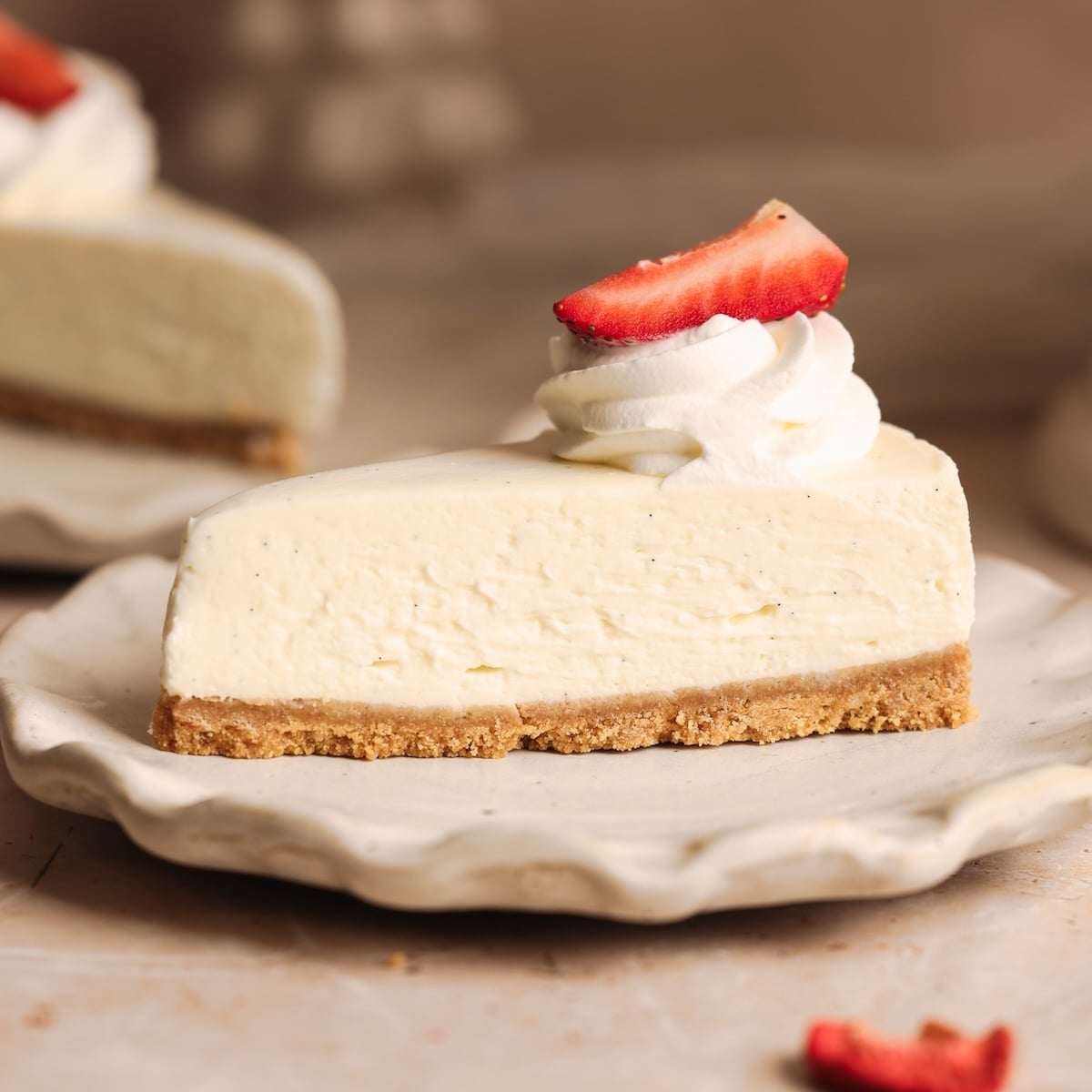 A slice of creamy, best no-bake cheesecake with a graham cracker crust, topped with a swirl of whipped cream and a sliced strawberry, sits on a white plate.