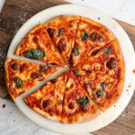 overhead image of pizza margherita on a round marble serving board. pizza has a crispy crust, melted cheese and basil leaves on it. one slice has been pulled out