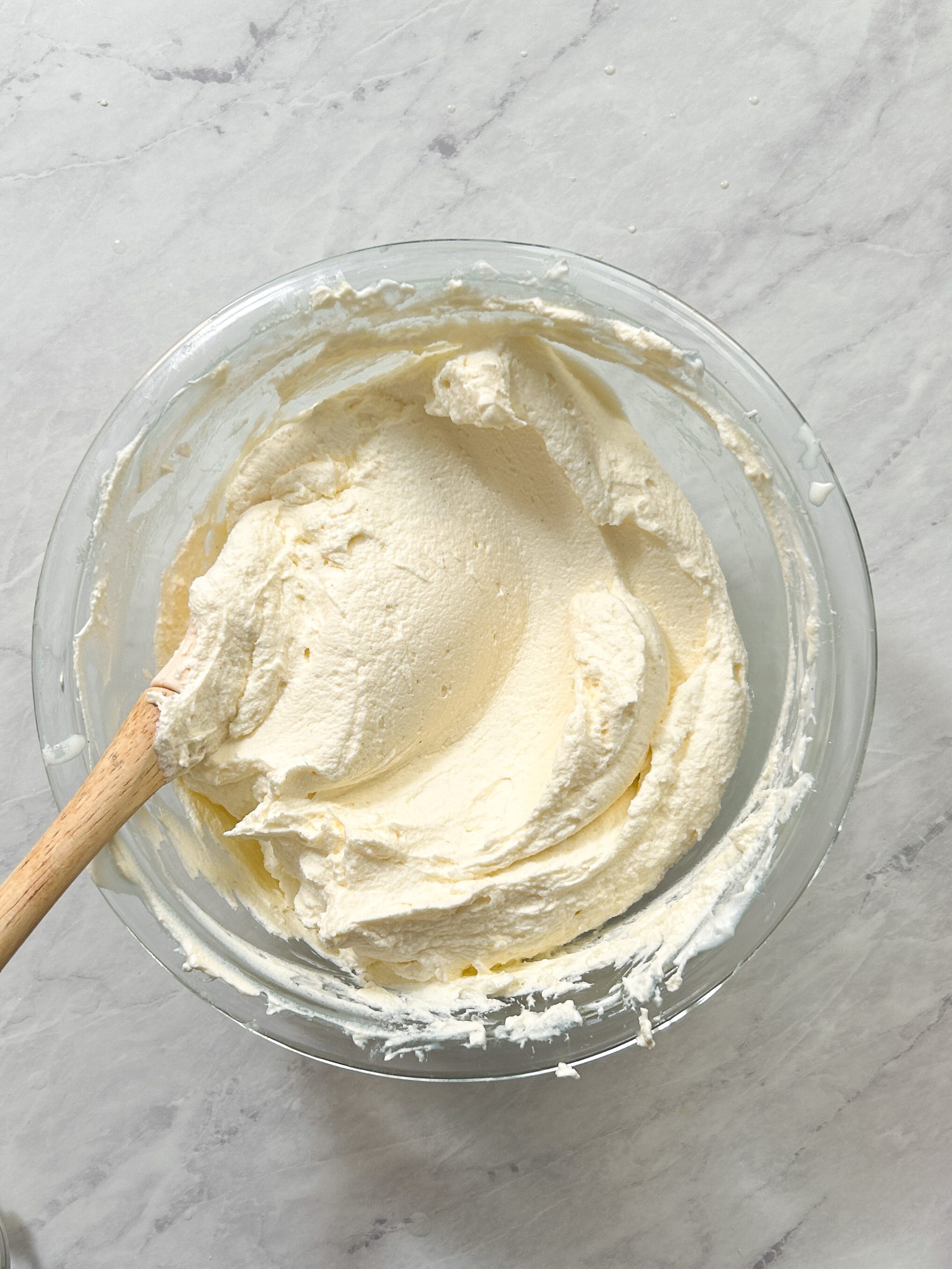 thick and fluffy mascarpone cream mixture in a glass bowl with a rubber spatula inside