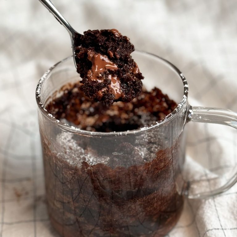 Molten Lava Chocolate Mug cake in a glass mug, with a small spoon taking out a bite revealing moist texture and molten chocolate instead
