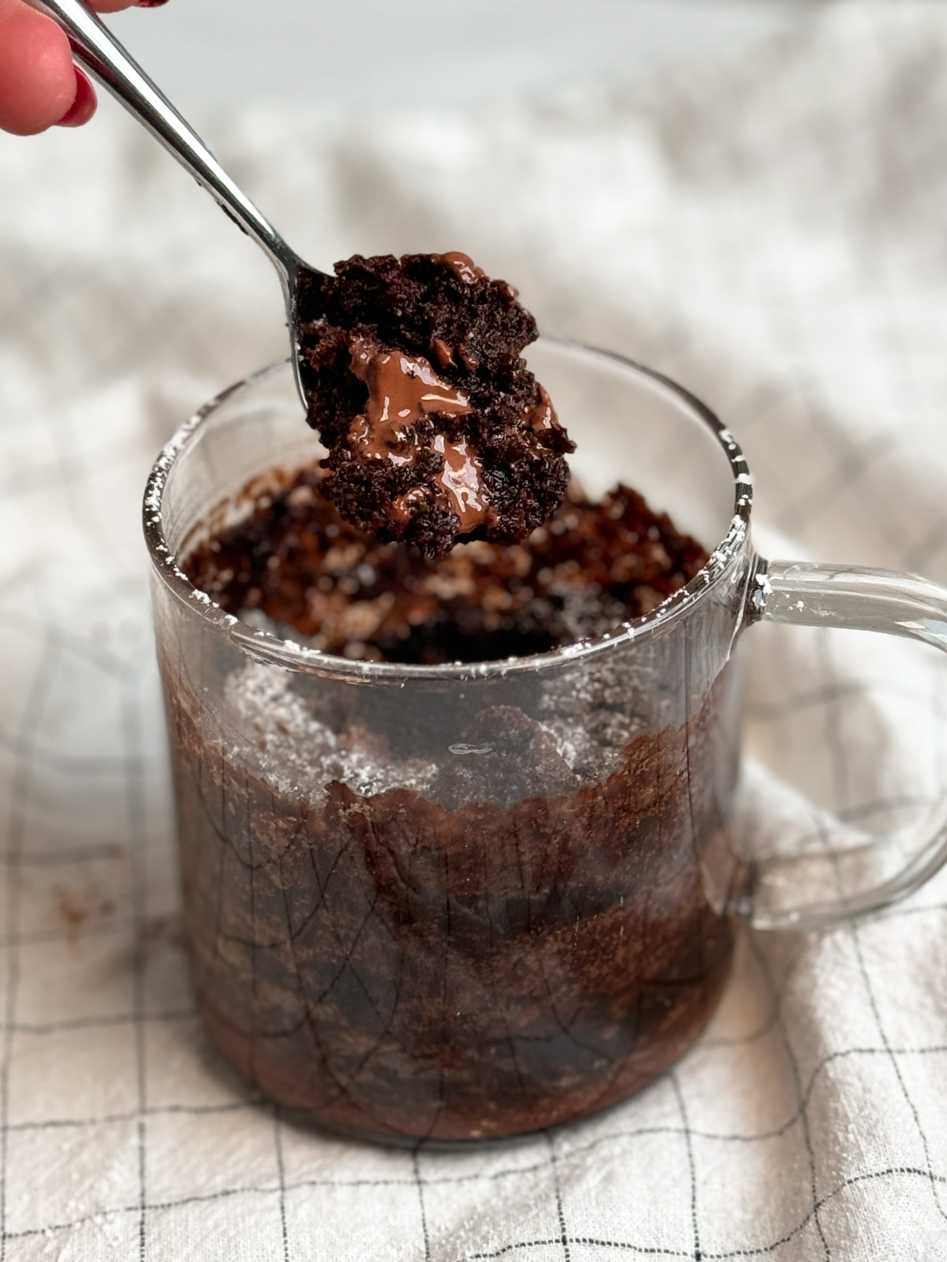 Molten Lava Chocolate Mug cake in a glass mug, with a small spoon taking out a bite revealing moist texture and molten chocolate instead