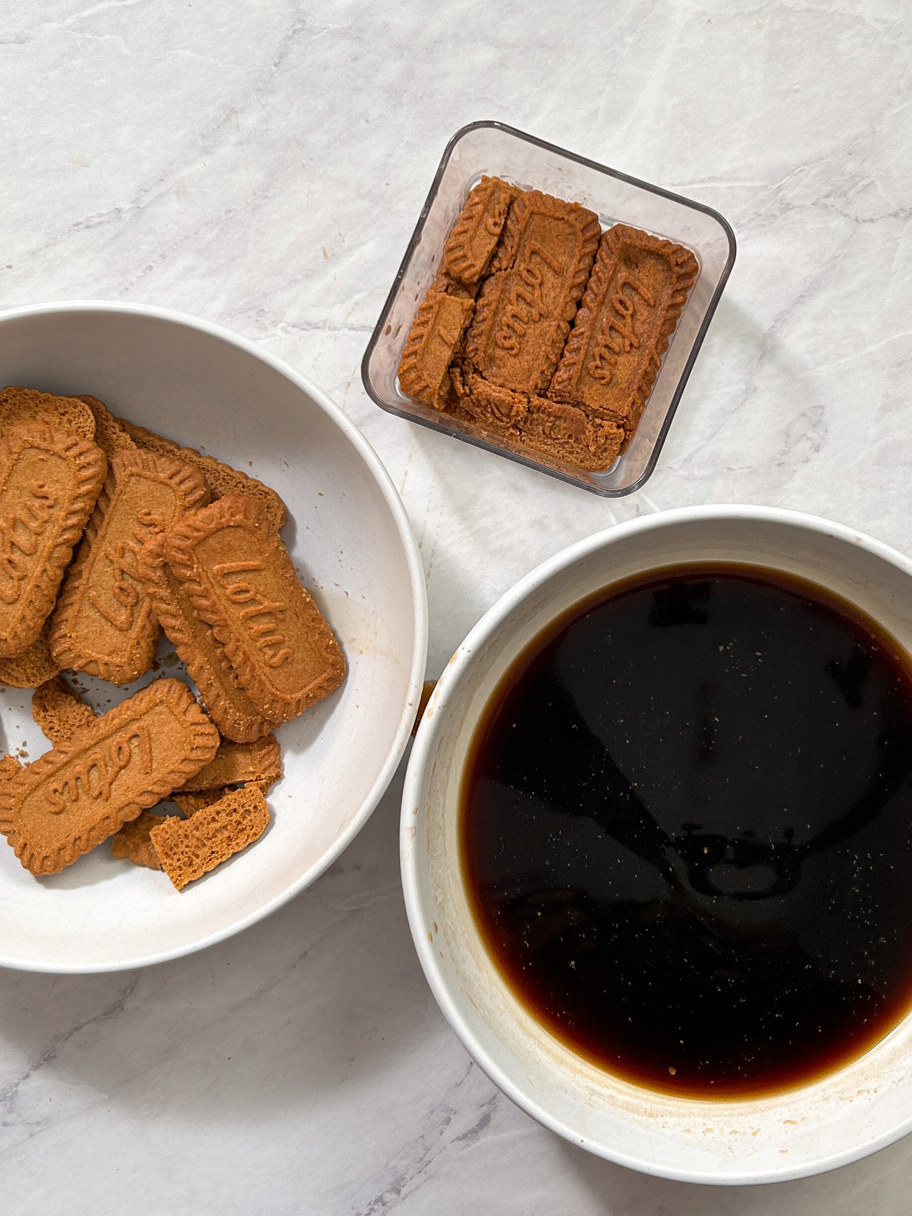 a plate with biscoff cookies, a bowl with coffee, and a dessert cup with a layer of soaked biscoff cookies