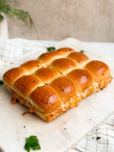 12 pull apart cheesy bbq chicken sliders made with kings hawaiian sweet hawaiian rolls on a marble serving board with the cheese oozing out from the side. pic from far