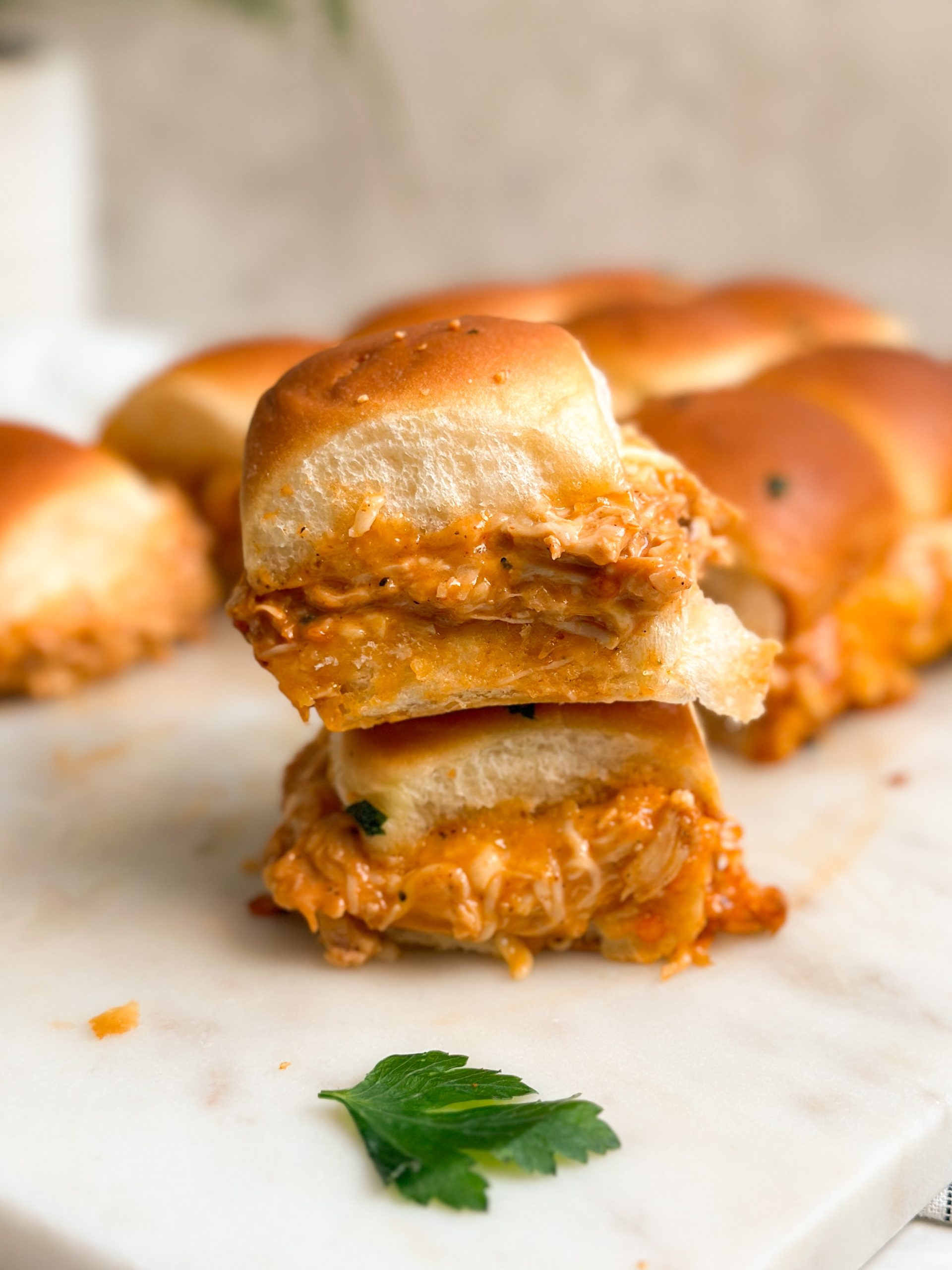 2 bbq chicken sliders stakced on top of each other with cheese oozing out, more in the background