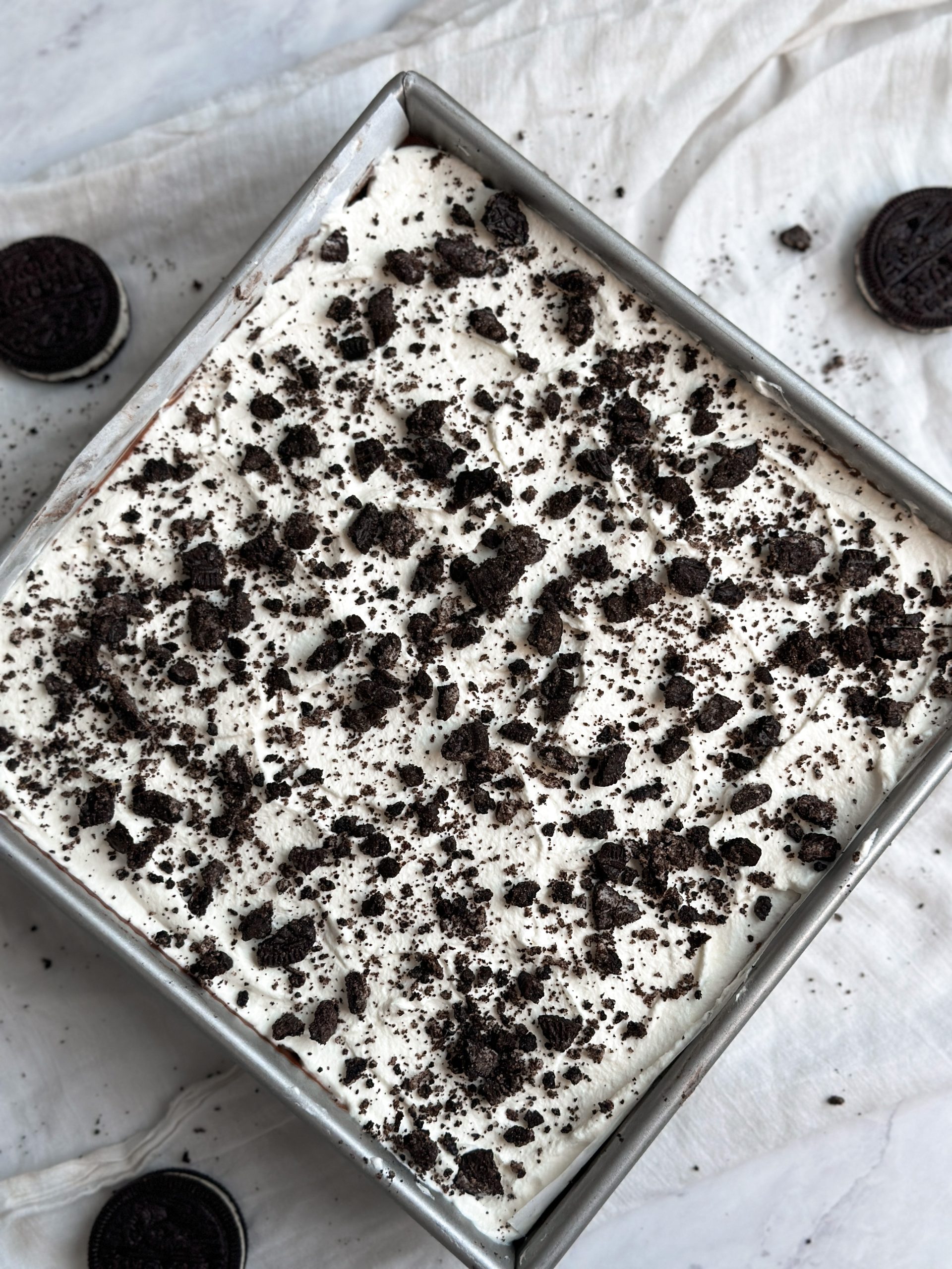 no bake cookies and cream (oreo) mousse cake in a square baking pan decorated with whipped cream and crushed oreos
