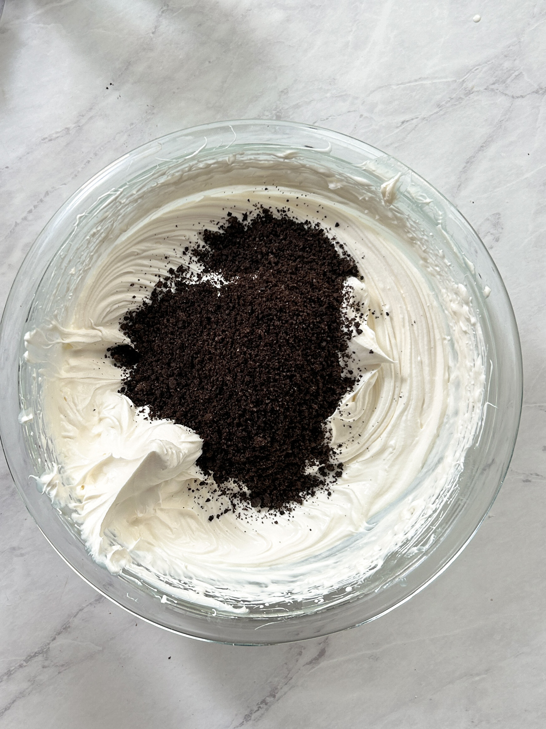 crushed oreo (chocolate cream) cookies on top of whipped cream in a glass bowl