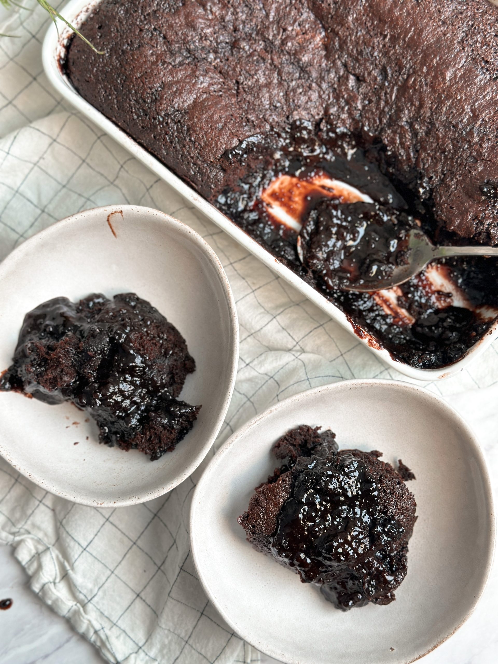 hot fudge chocolate cake in a ceramic dish with 2 spoon pulled out into 2 bowl revealing layer of hot fudge sauce under the cake. cake is moist and rich and saucy
