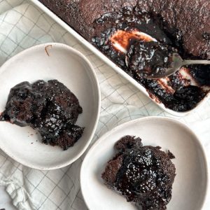 hot fudge chocolate cake in a ceramic dish with 2 spoon pulled out into 2 bowl revealing layer of hot fudge sauce under the cake. cake is moist and rich and saucy