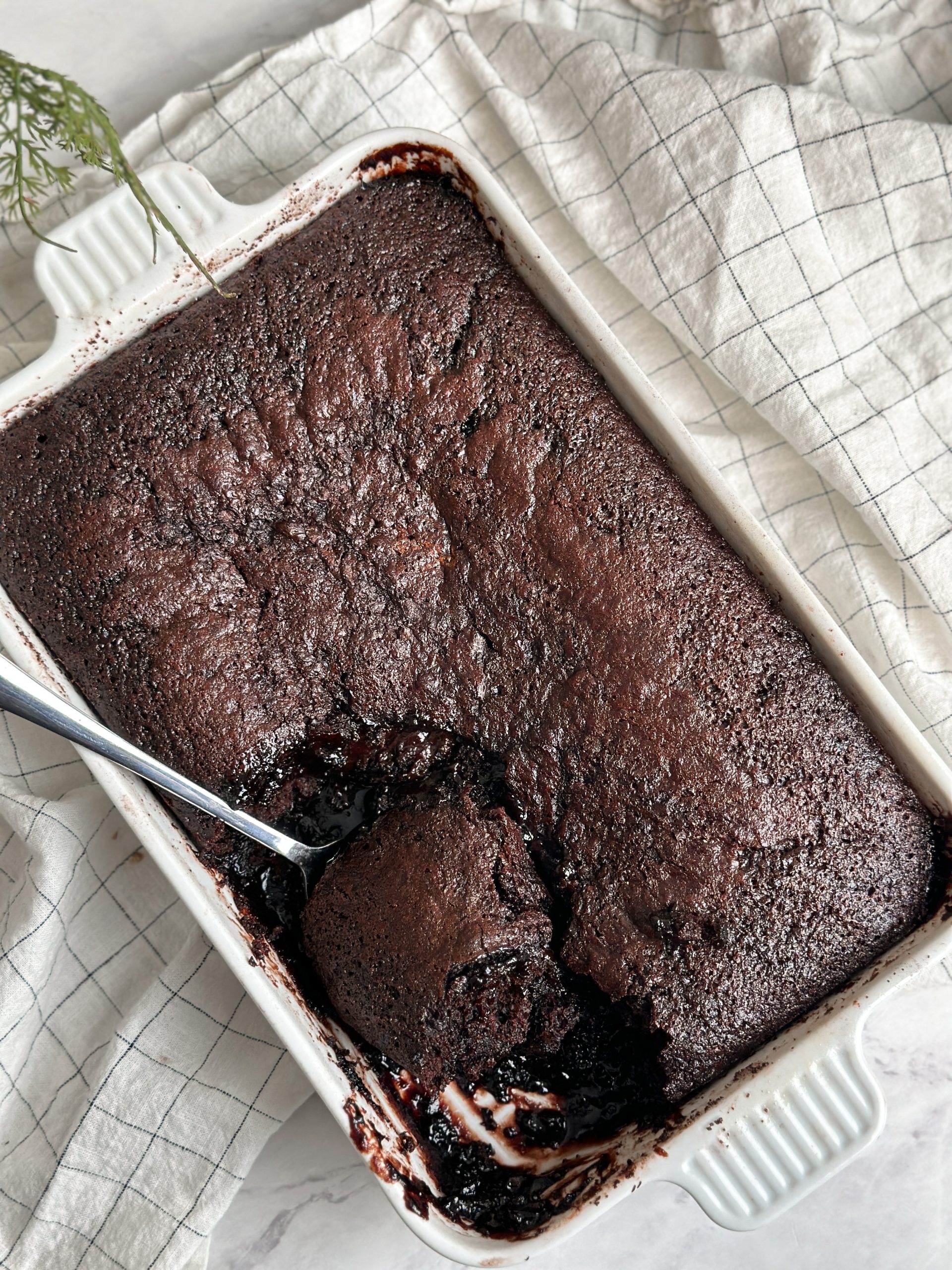 hot fudge chocolate cake in a ceramic dish with a spoon pulling out a serving revealing a layer of hot fudge underneath the chocolate cake, pic from the top