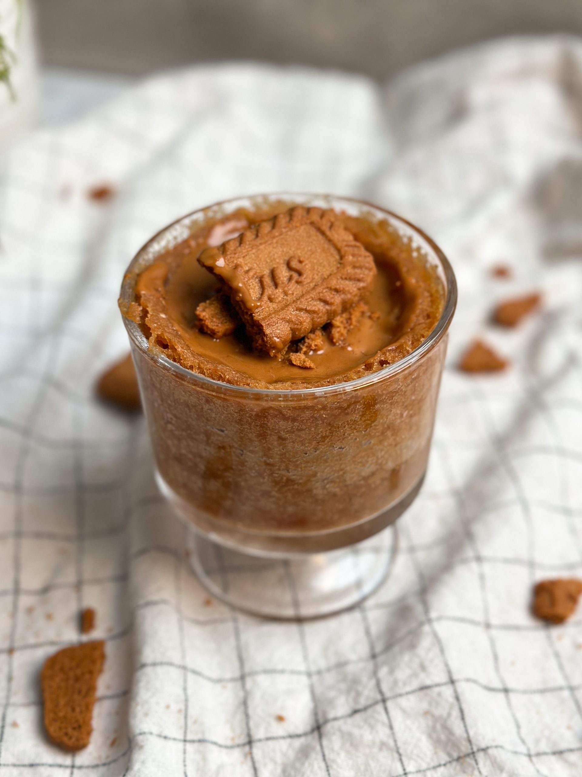 Side picture of a Biscoff mug cake in a glass mug, covered in biscoff cookie butter and crushed cookies