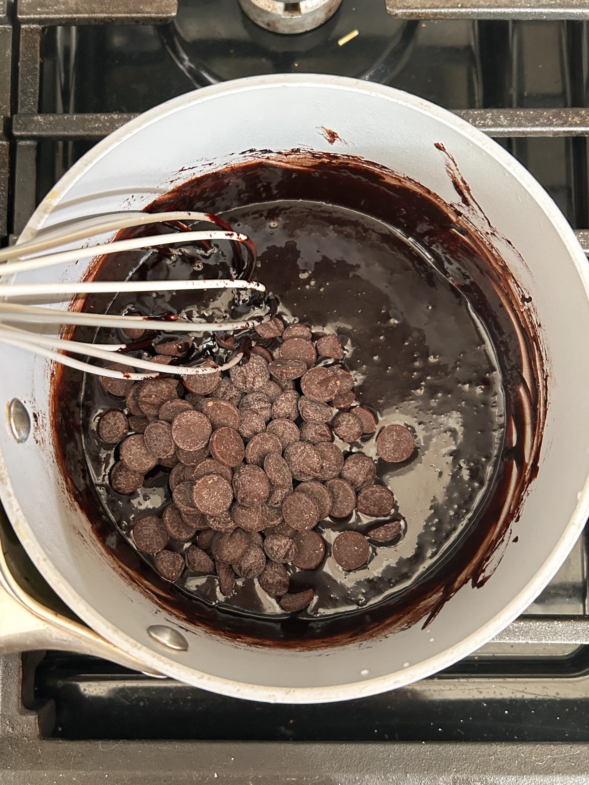 chocolate chips added to chocolate sauce in a saucepan with a whisk