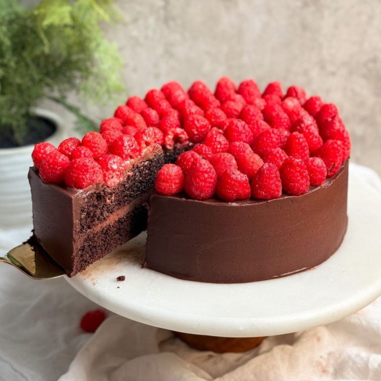 Chocolate raspberry fudge cake on a marble serving board with a spatula pulling out a slice revealing moist chocolatey interior, chocolate ganache, and layer of raspberries on top