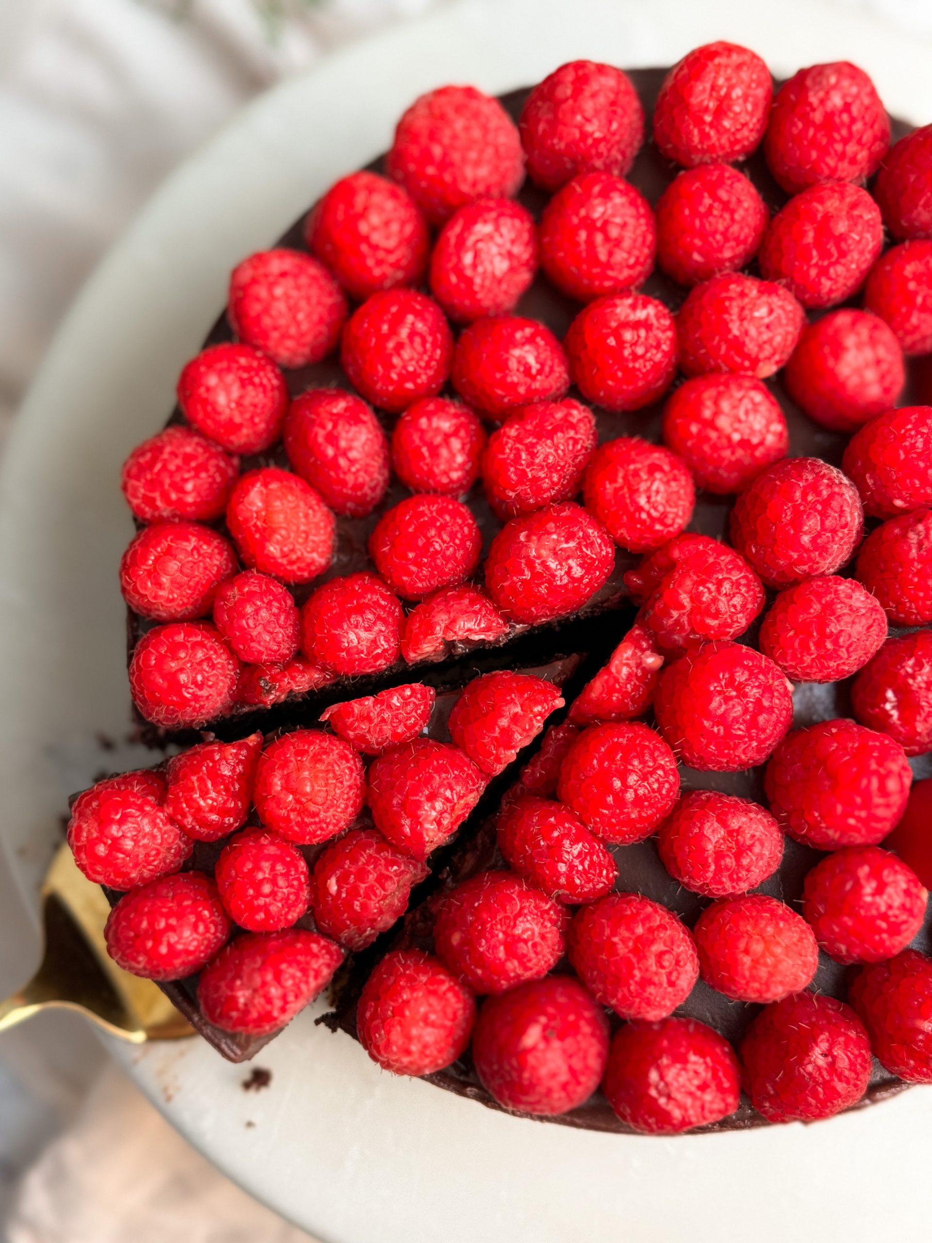 Overhead picture of a chocolate cake covered with raspberries with 1 slice being pulled out