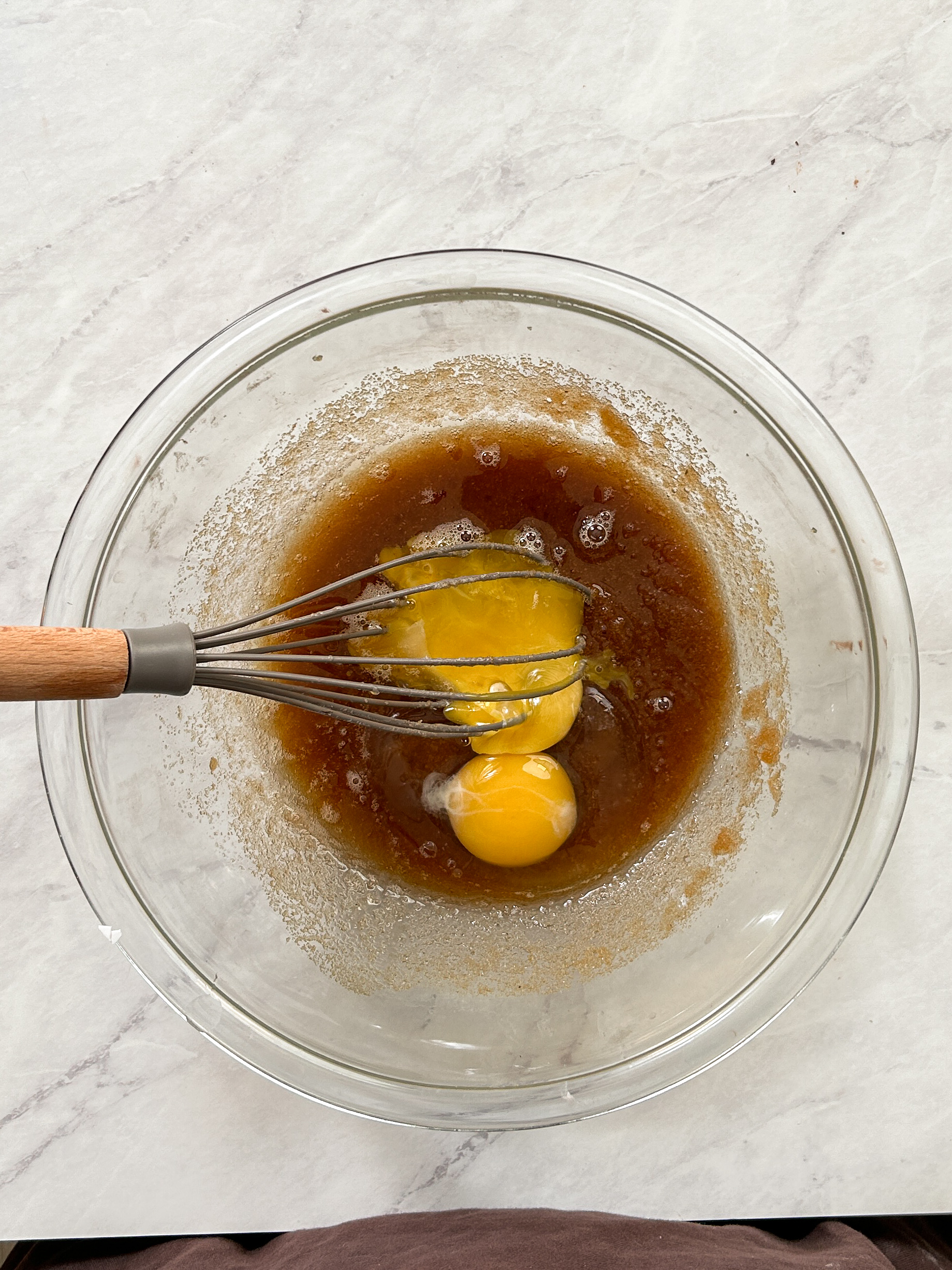 eggs added to butter and sugar mixture in a glass bowl with a whisk inside